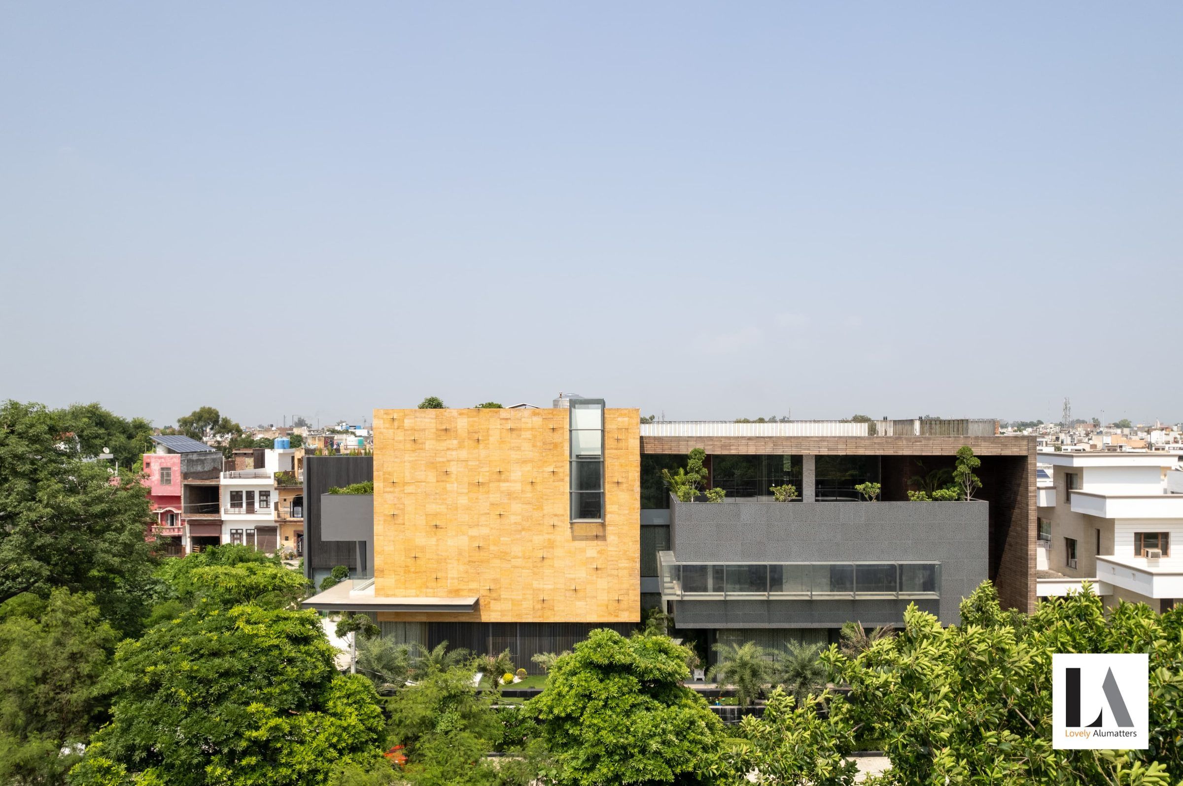 Aerial view of the residence set among trees, with ribbon glazing beneath a stone-clad volume