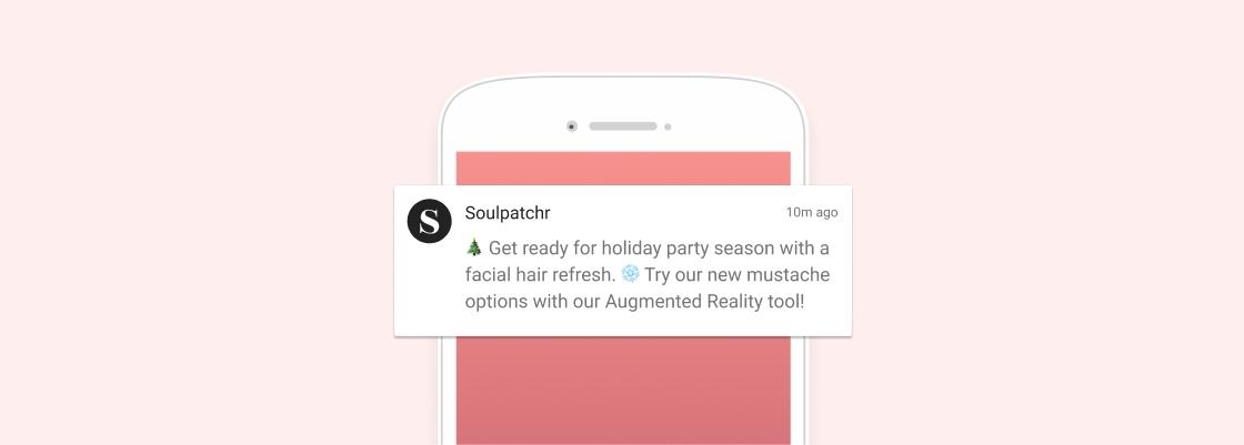 A smartphone displays a notification from Soulpatchr about holiday party preparations and new mustache options using Augmented Reality. The background is a soft pink color.
