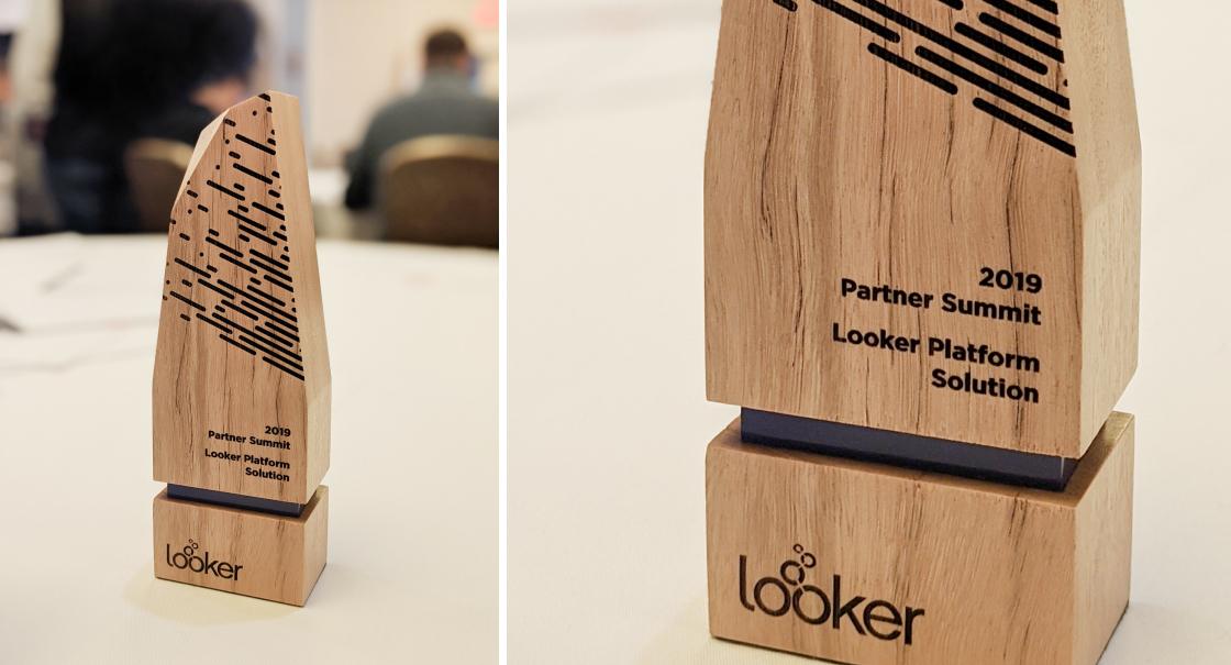 A wooden award trophy with "2019 Partner Summit Looker Platform Solution" engraved on it. The trophy features a modern design with black lines and the Looker logo.