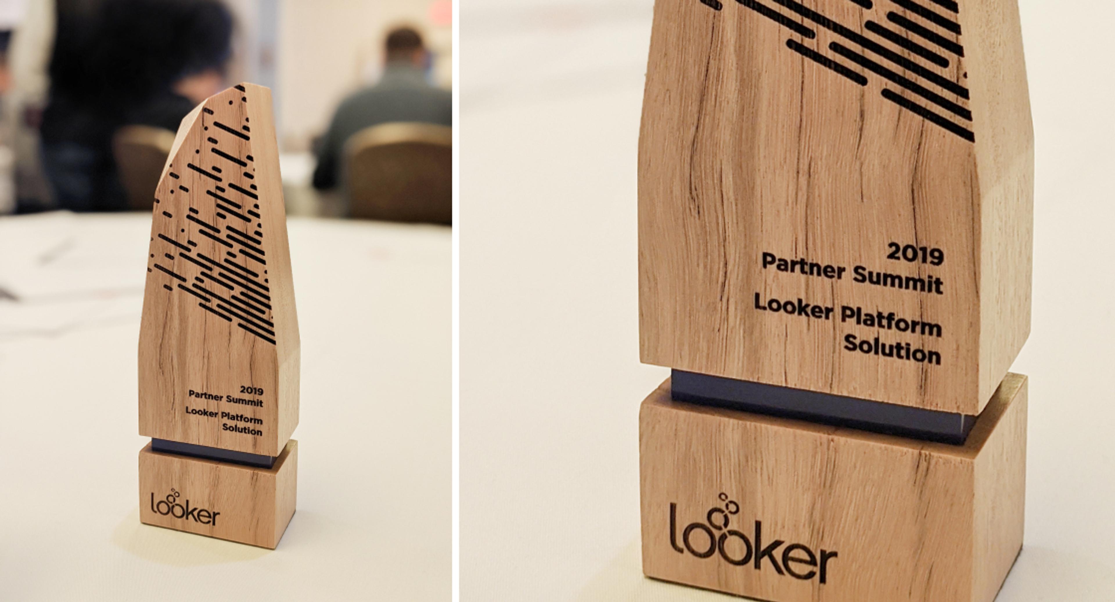 A wooden award trophy with "2019 Partner Summit Looker Platform Solution" engraved on it. The trophy features a modern design with black lines and the Looker logo.