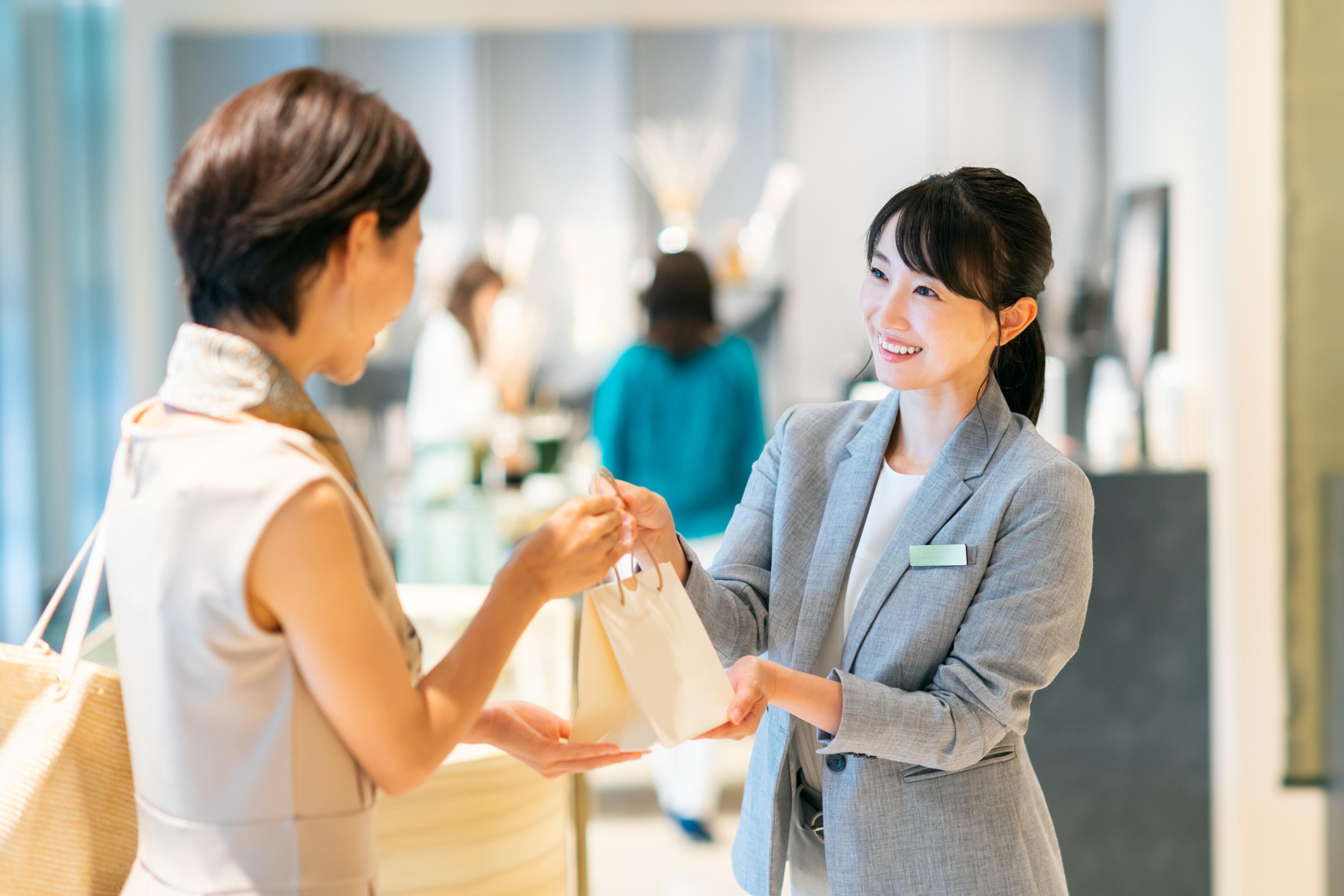 店員が顧客に小さな袋を渡しているシーン。明るい店内でのやり取り。