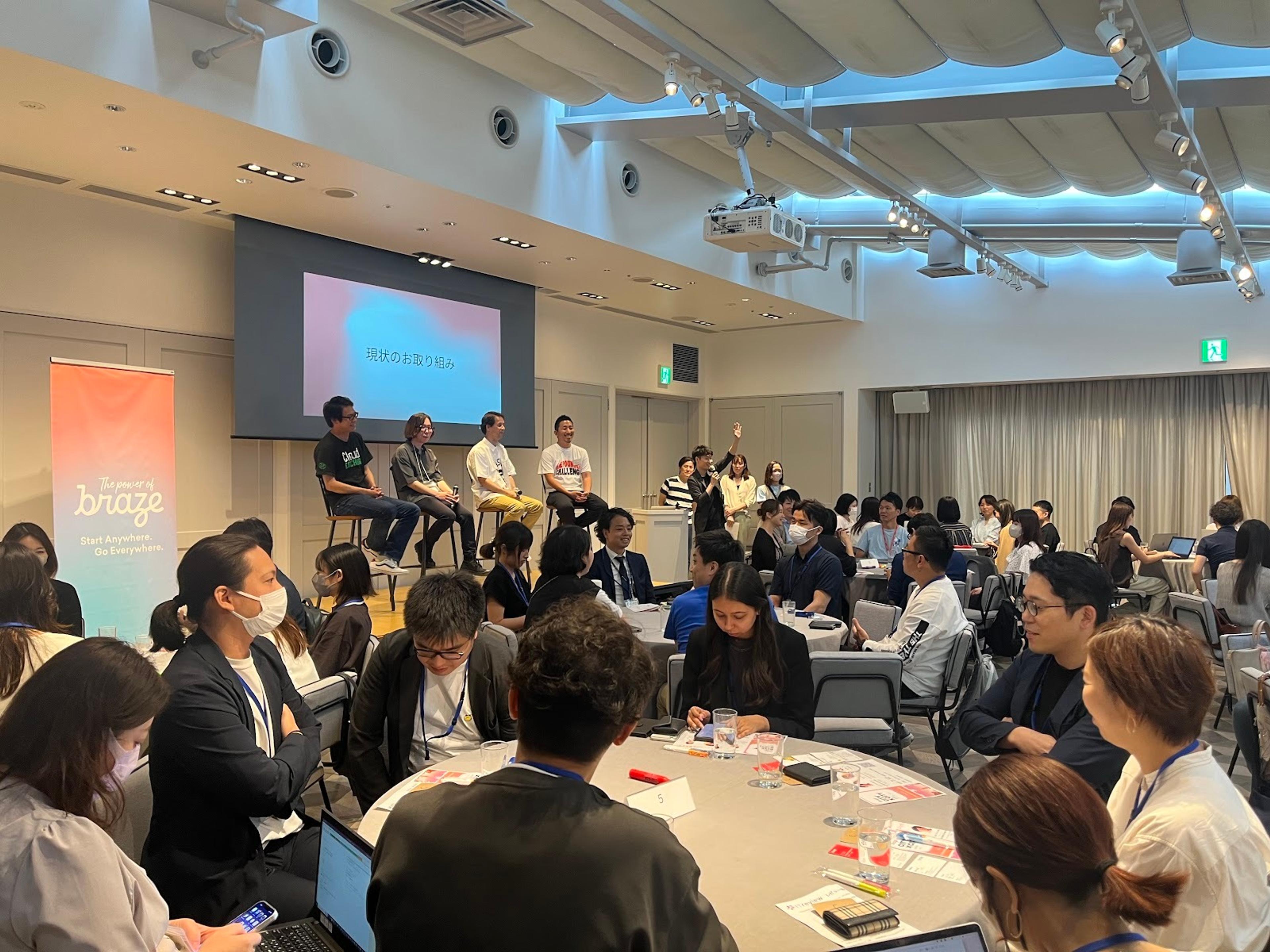 会議室でのイベントの様子。参加者が座っており、パネリストがステージで話しています。