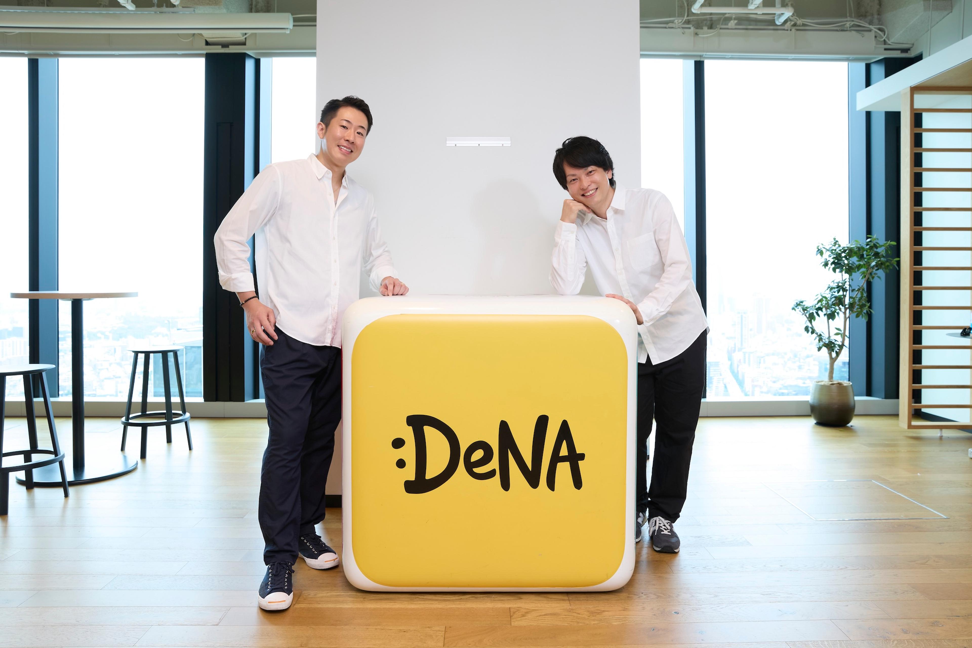 DeNAのロゴの前で二人の白いシャツをきた男性が立っている