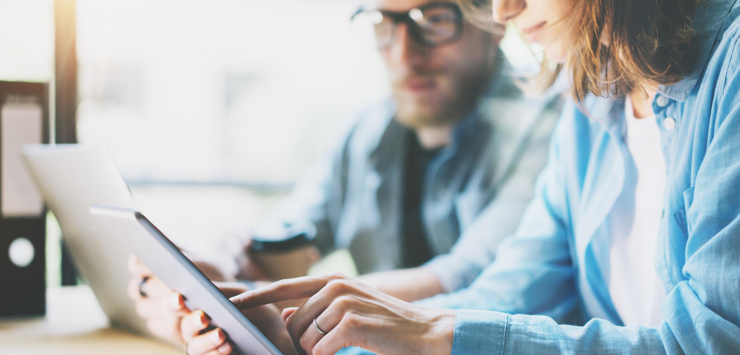 Woman using a tablet, man in background.
