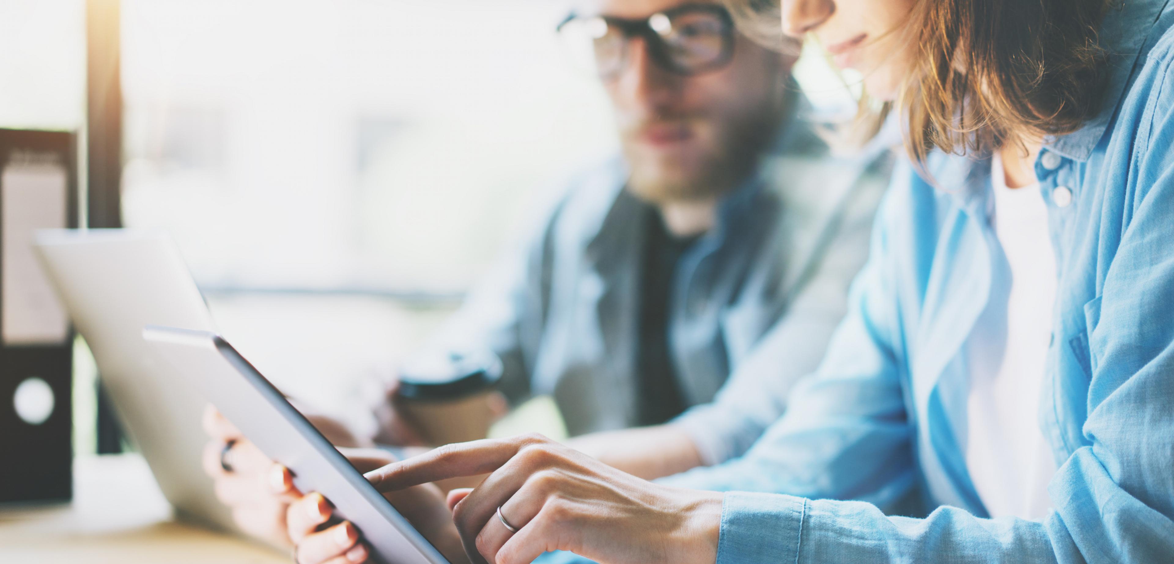 Woman using a tablet, man in background.