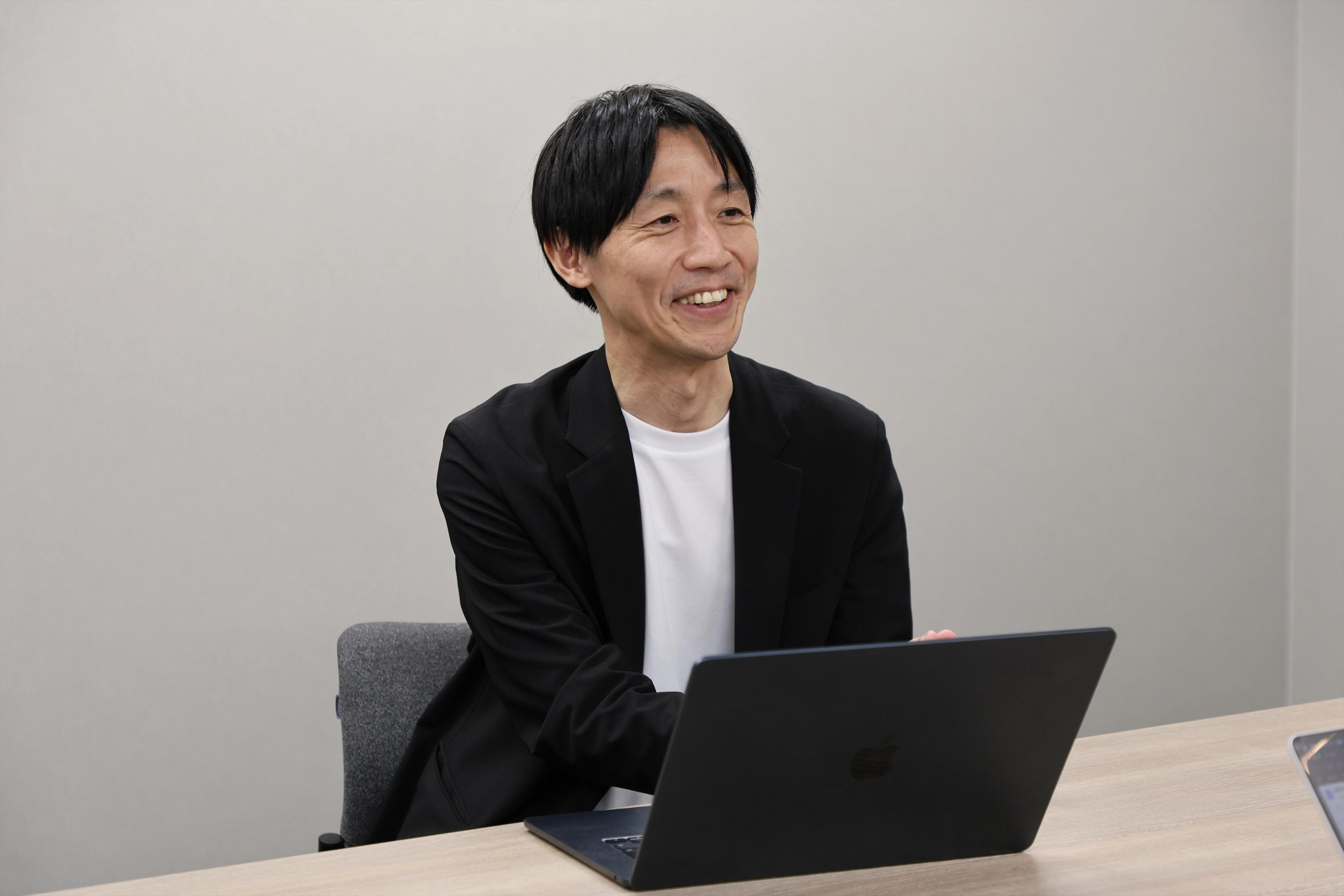 サツドラホールディングス株式会社 CDO兼株式会社サッポロドラッグストアー OMO本部本部長兼マーケティング部ゼネラルマネージャーの坂本 武史さんがインタビューを受けている様子。PCを前に笑顔で話をしている
