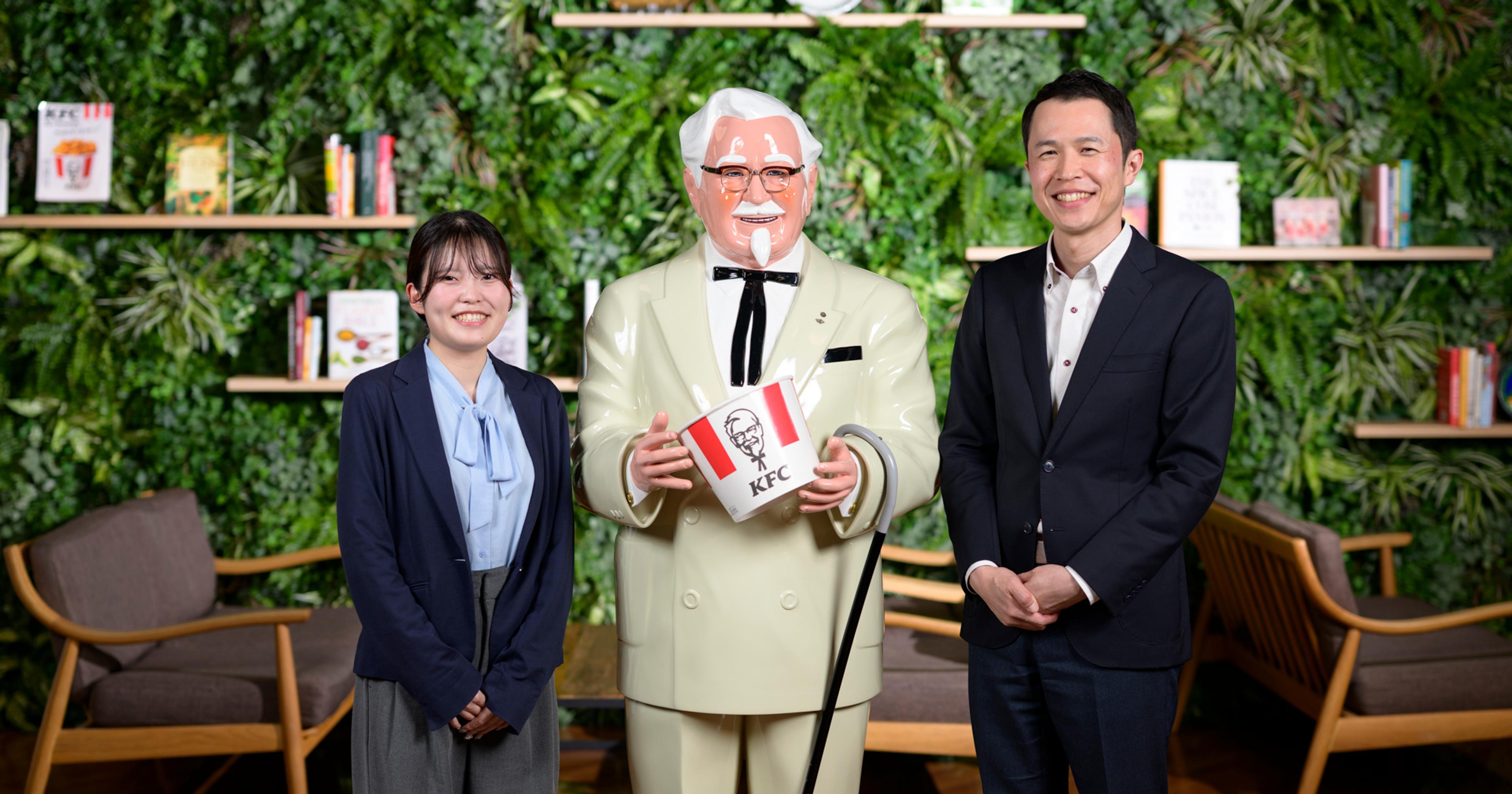 インタビューに答えた野中さんと平田さんがカーネルサンダースを挟んで並んでいる