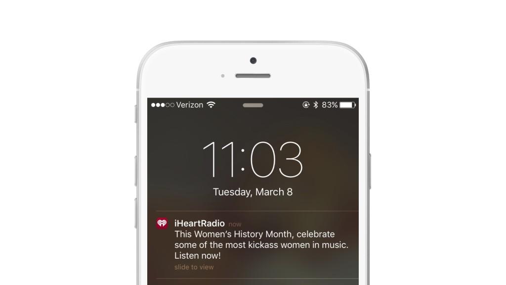 A smartphone screen displaying a notification from iHeartRadio about Women's History Month, encouraging listeners to celebrate women in music. The time is 11:03 on March 8.