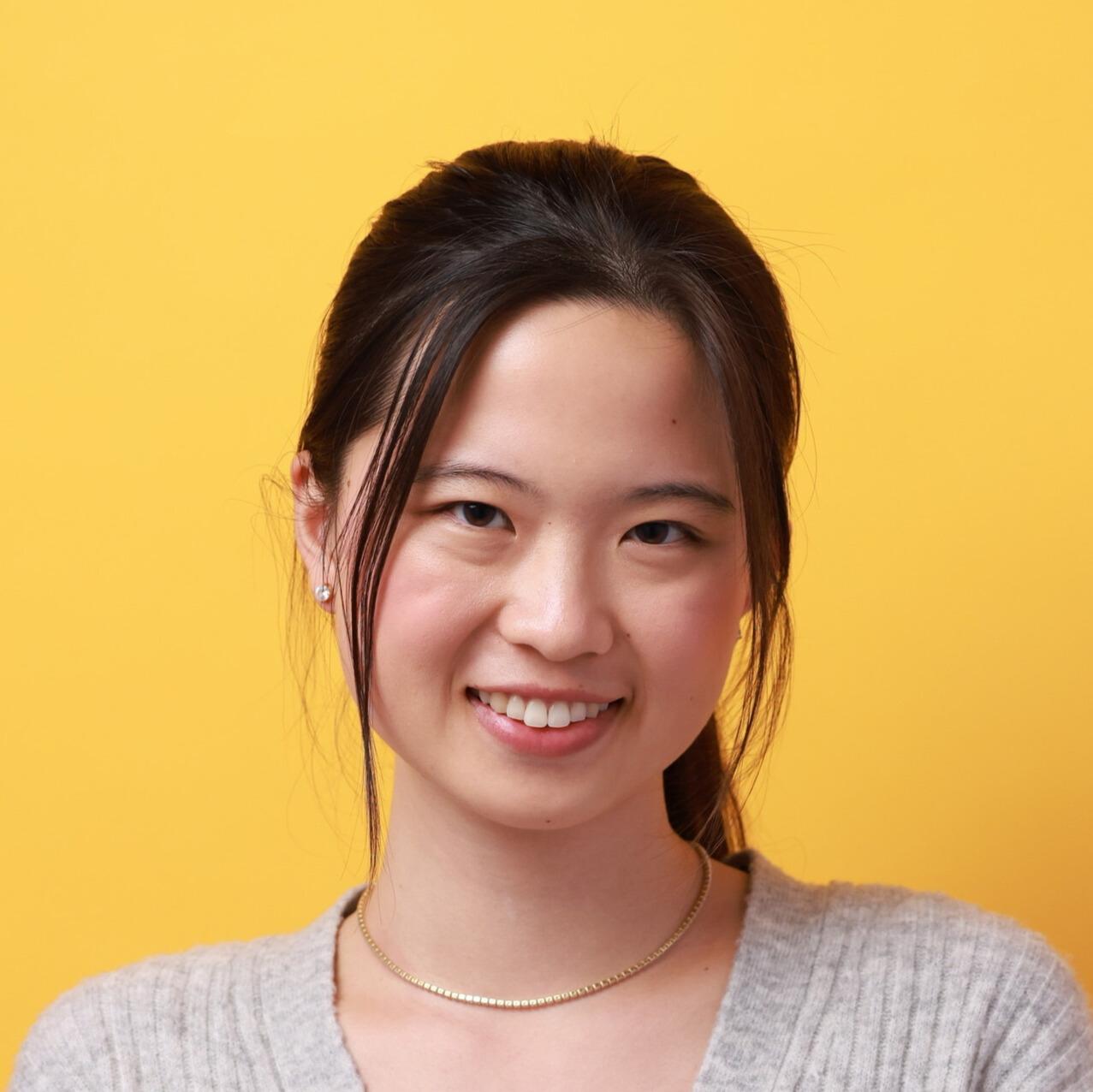 Headshot of a smiling young woman with dark hair against a bright yellow background.