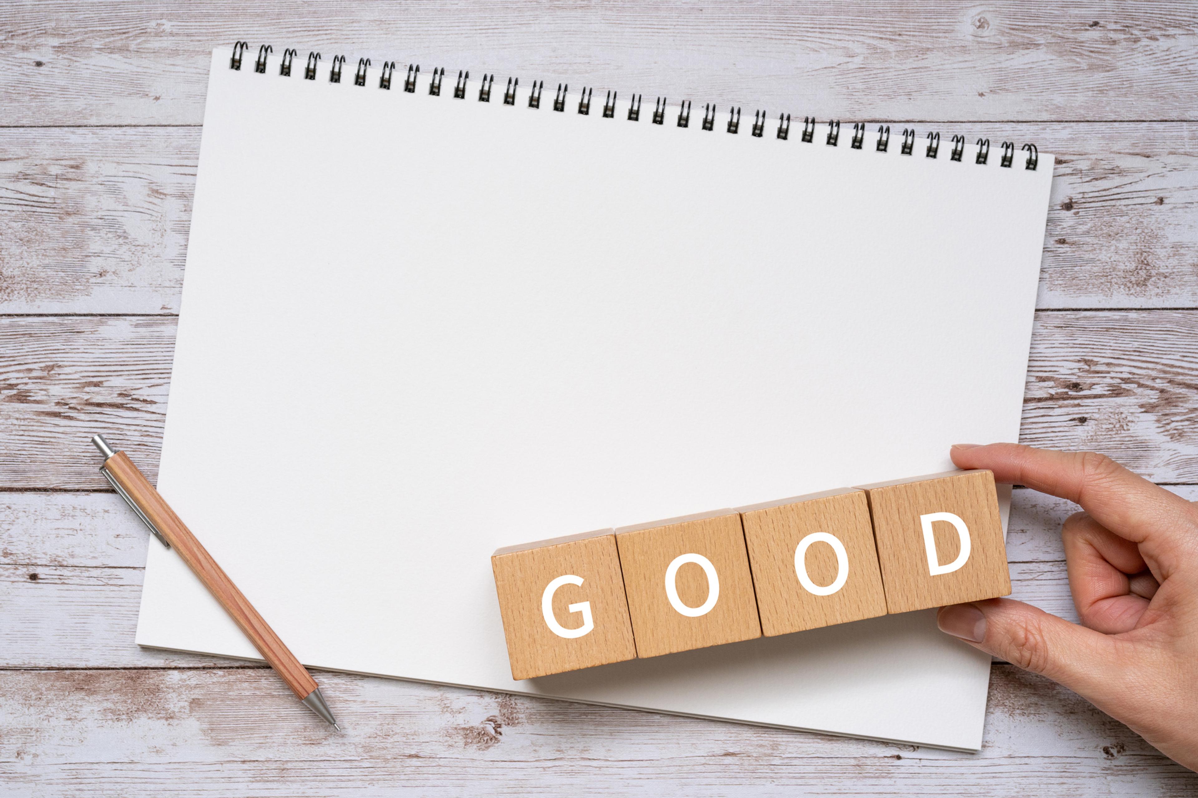 白いスケッチブックと鉛筆の横に「GOOD」と書かれた木製ブロックがあります。