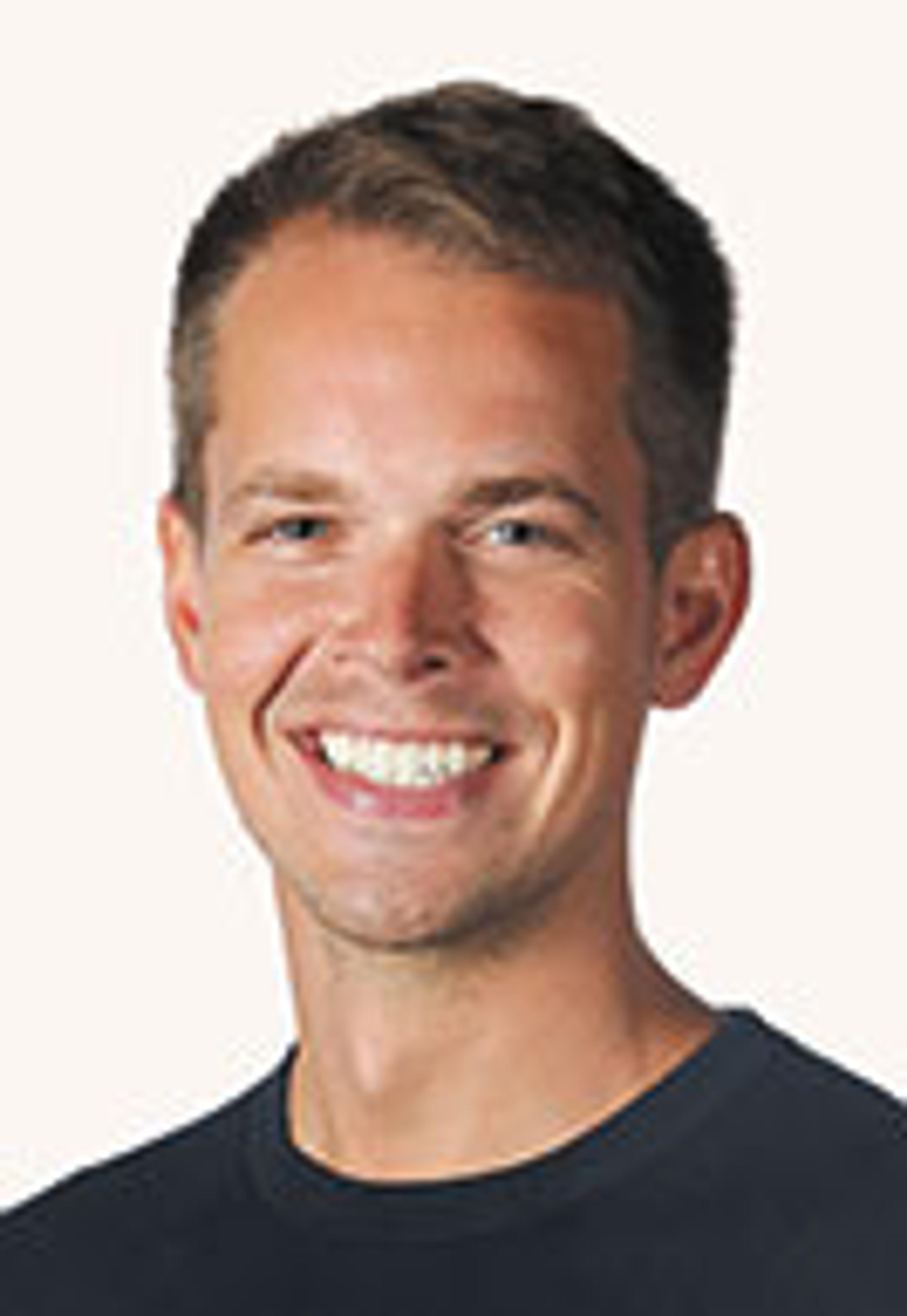 A smiling young man with short hair, wearing a dark shirt, against a light background.