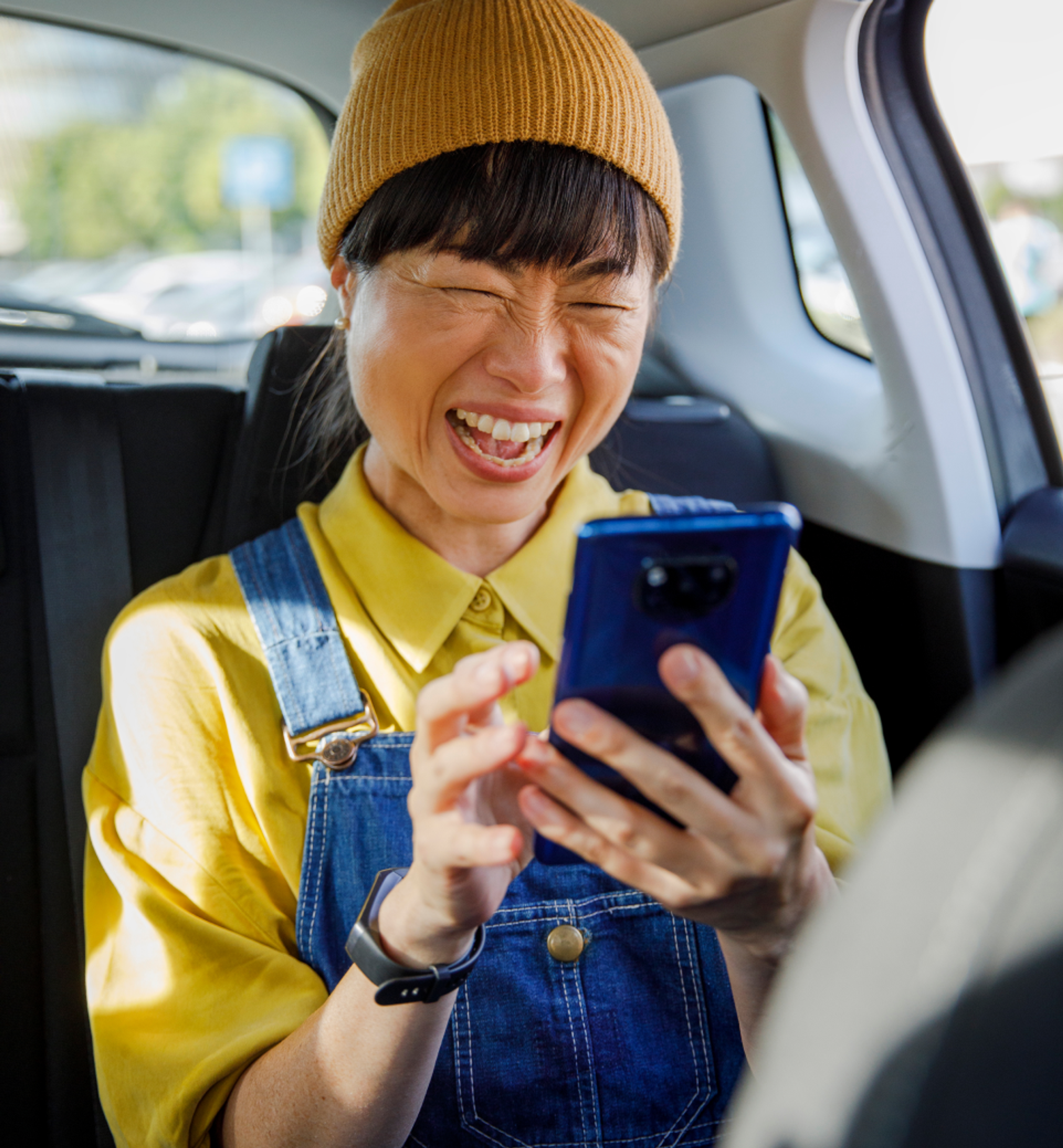 Person sitting in the back seat of a car laughing joyfully while looking at a smartphone.