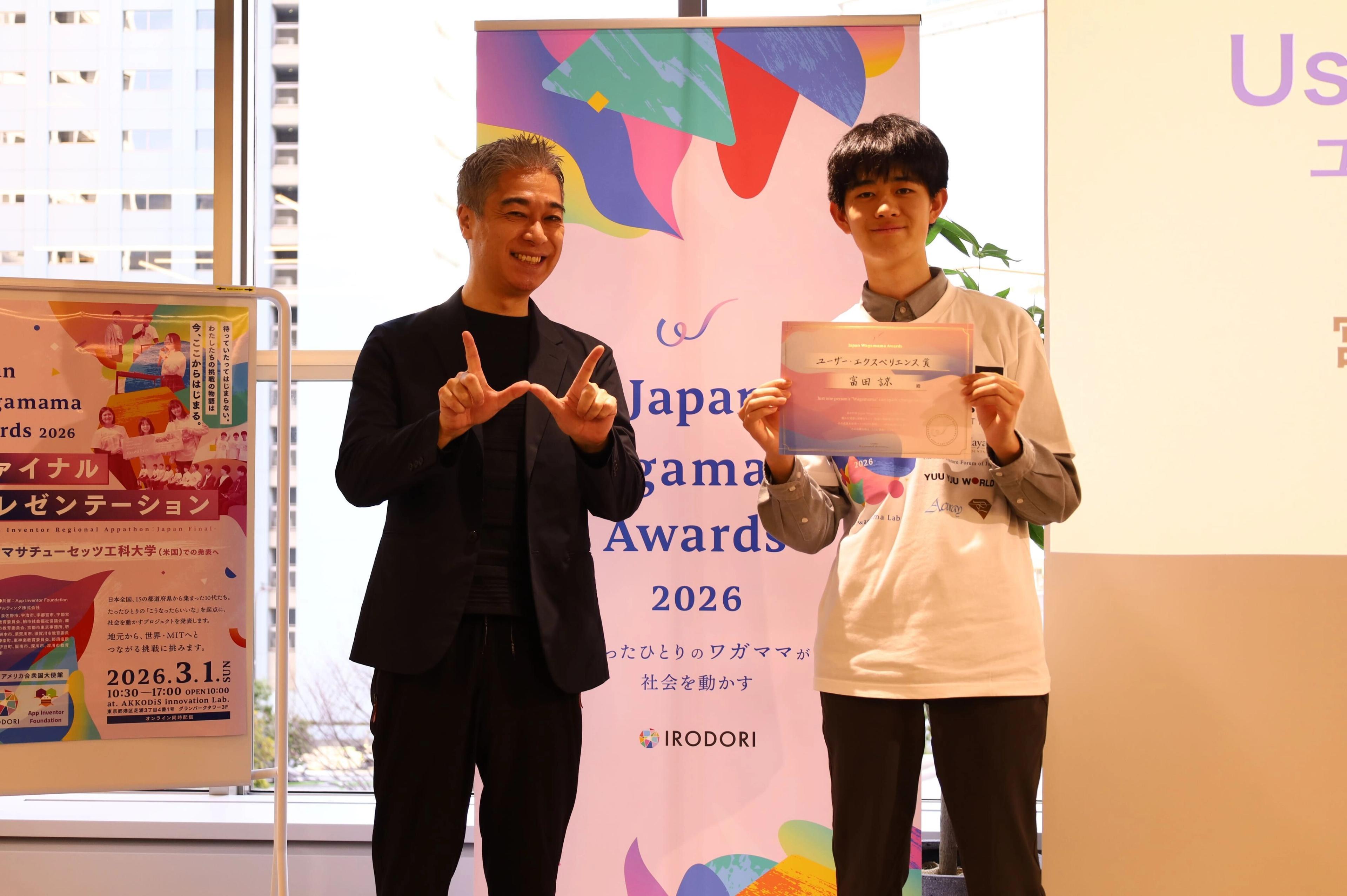 表彰式に出席した二人の男性：一人は笑顔で身振り手振りし、もう一人は表彰状を手にしている。