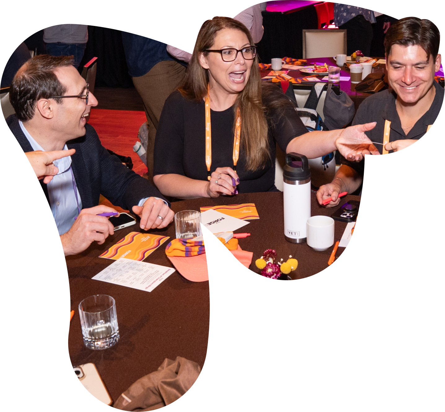 Three smiling people engaged in conversation around a table at an event.