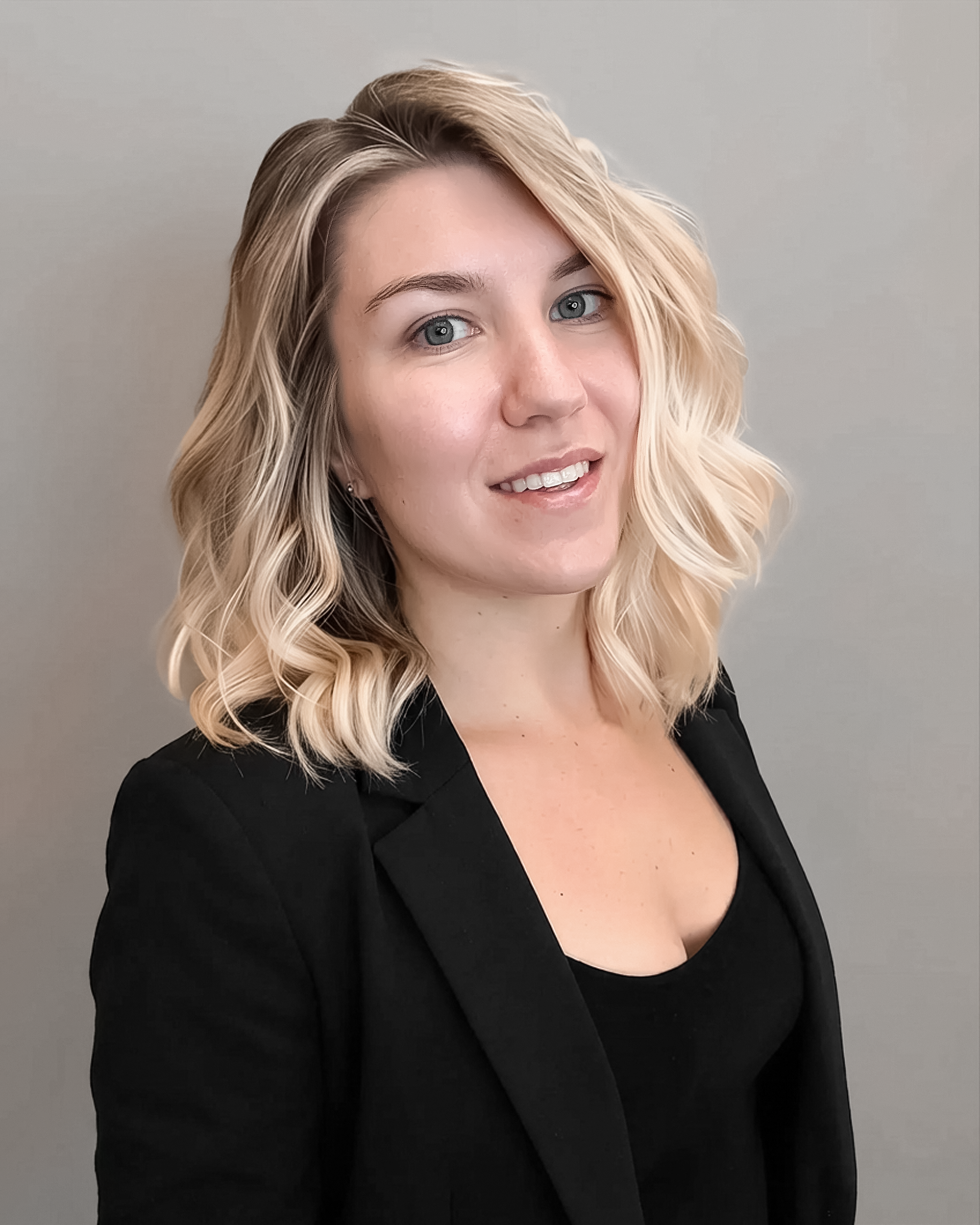 A woman with wavy blonde hair smiles at the camera, wearing a black blazer over a black top. The background is a light gray color.