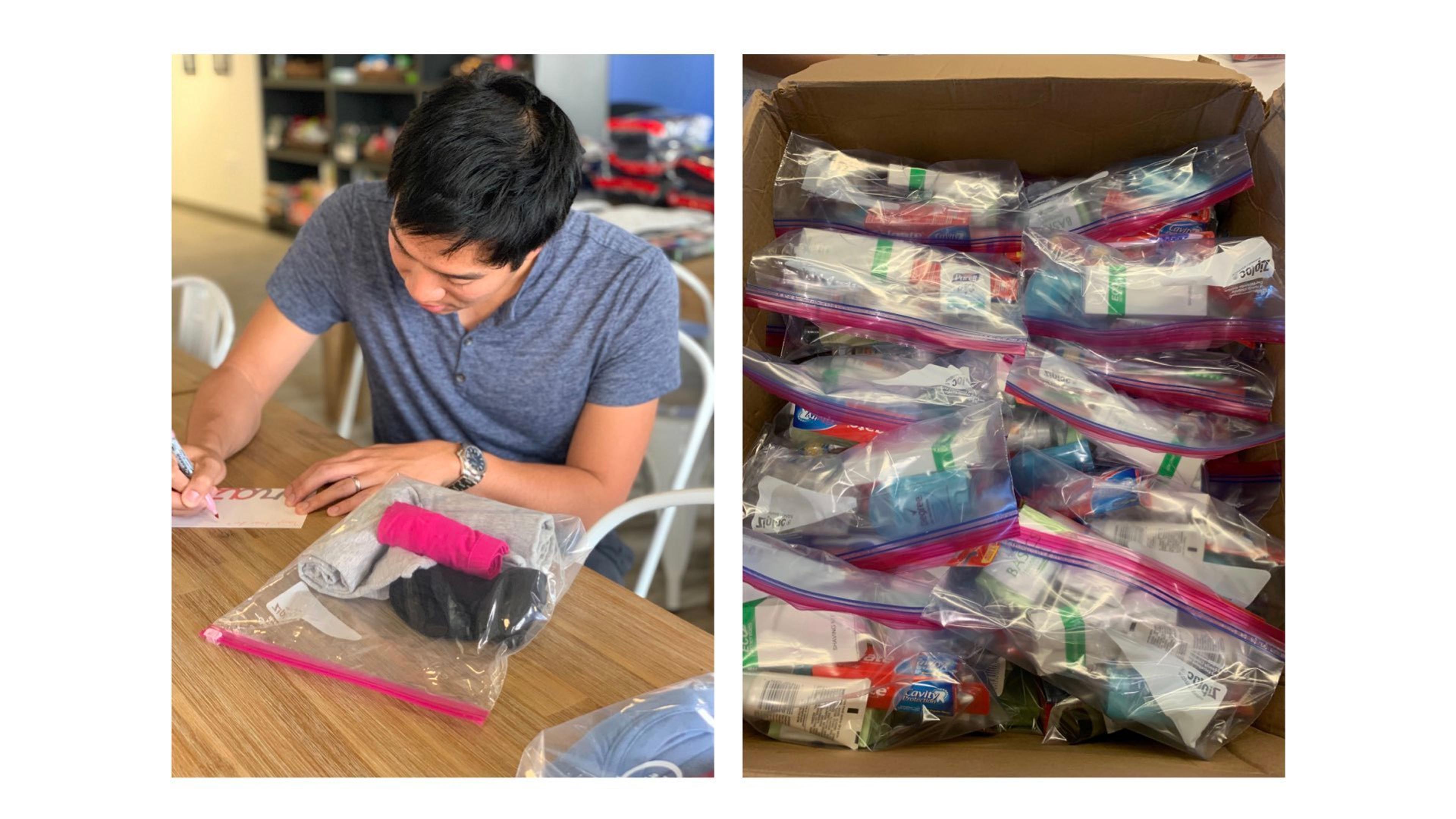 A person is writing on a card while sitting at a table. Next to them is a box filled with multiple ziplock bags containing various personal care items.