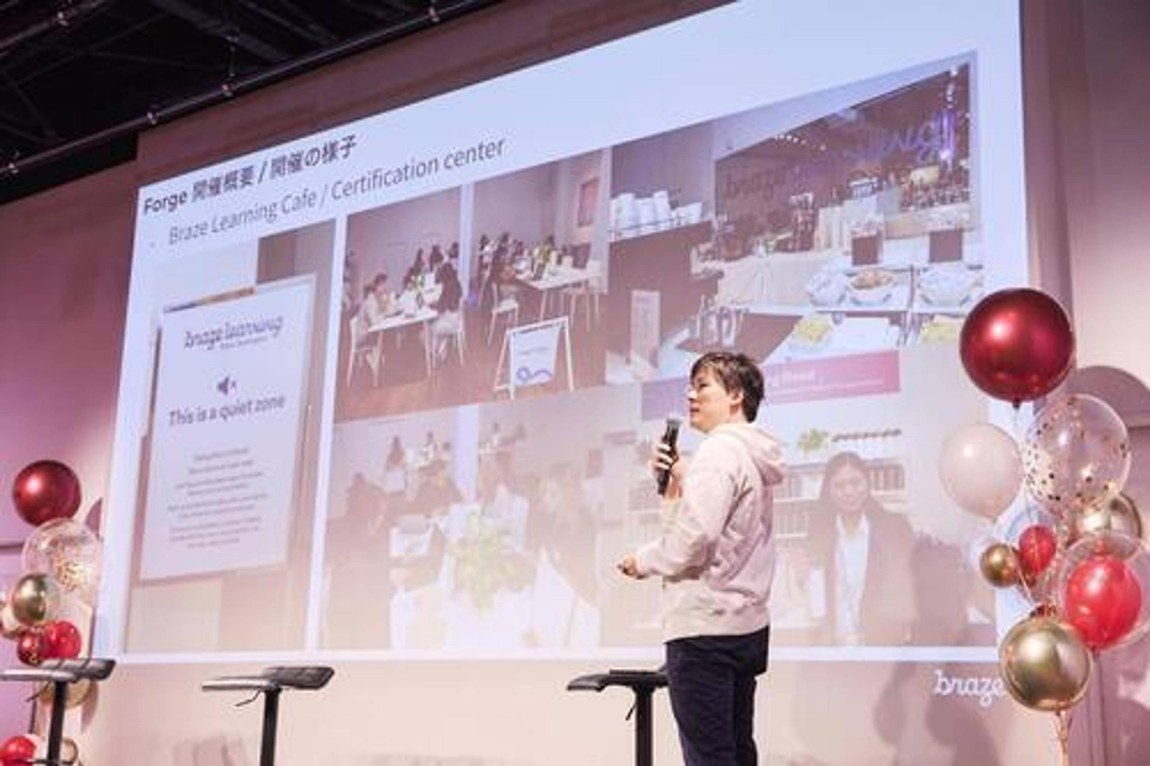 プレゼンテーションを行っている人物が、スライドを指し示しています。スライドには、ブレイズラーニングカフェと認定センターの写真が表示されています。