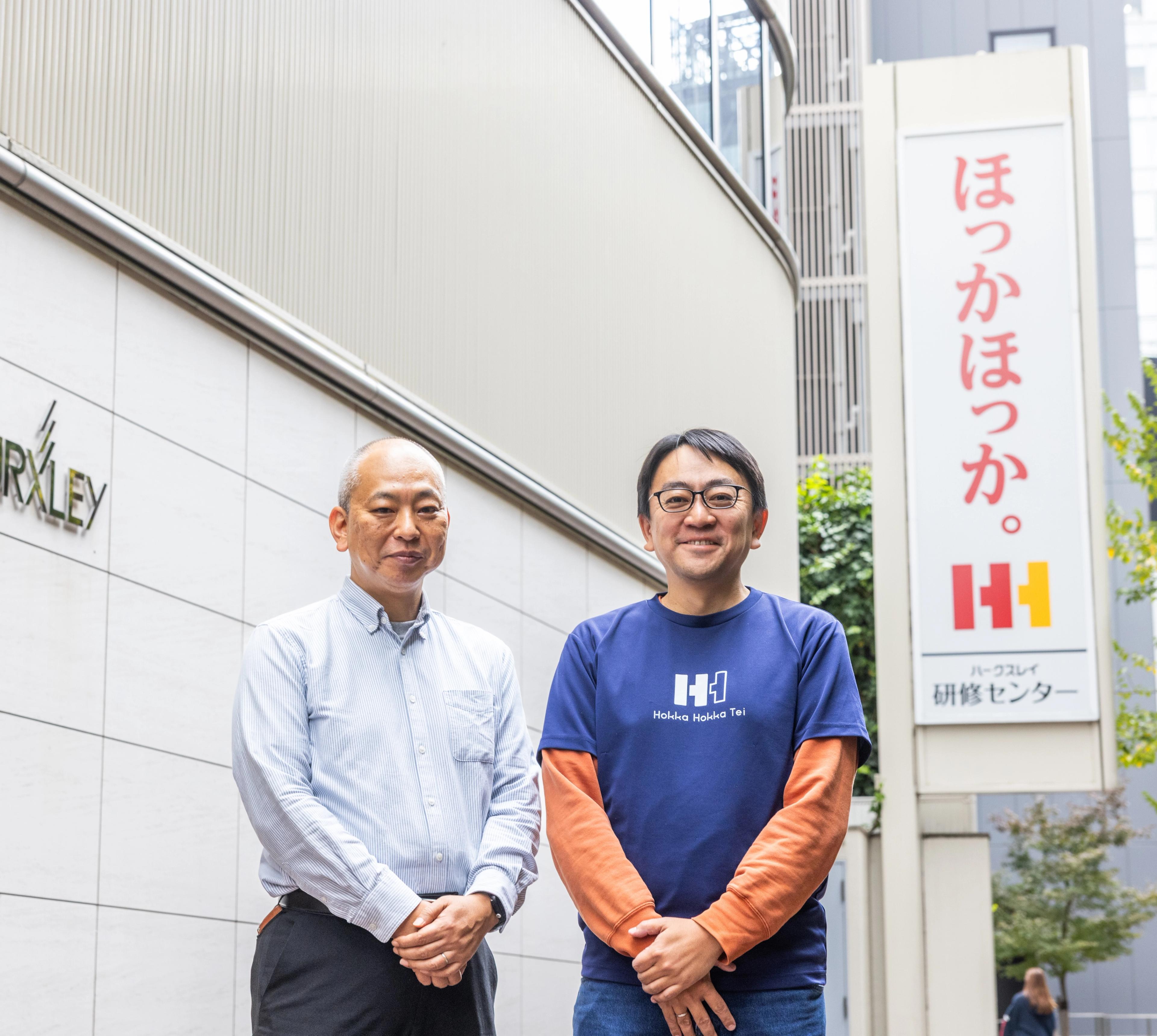 ほっかほっか。のロゴの前で男性二人が立っている。