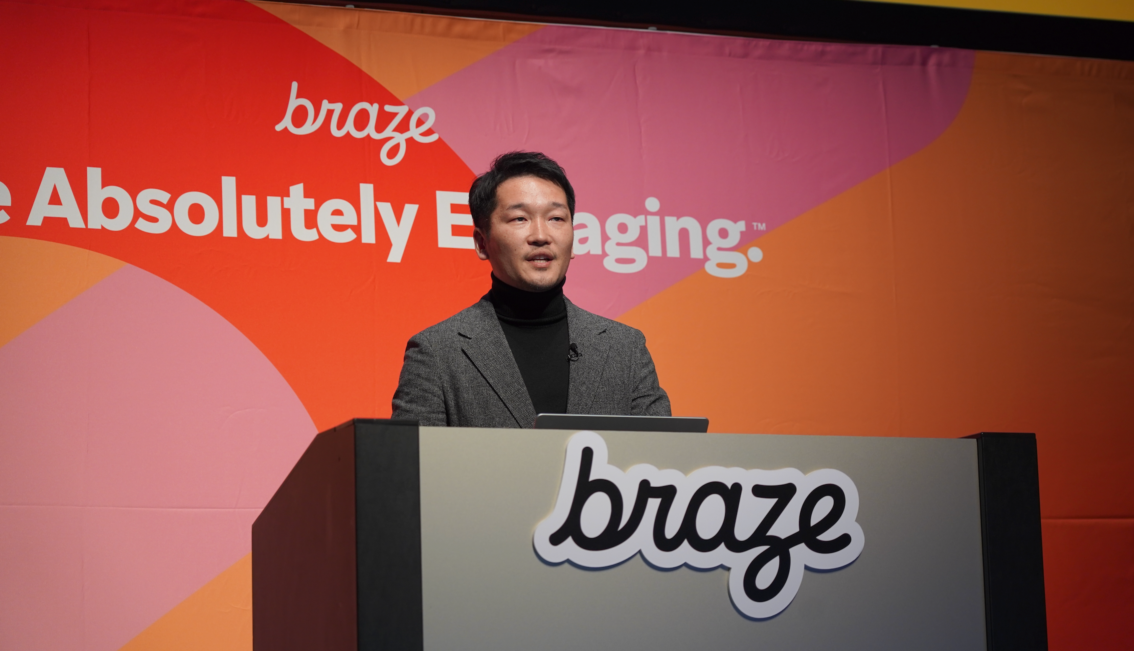 男性がプレゼンテーションを行っている様子。背景には「braze」のロゴとカラフルなデザインがある。