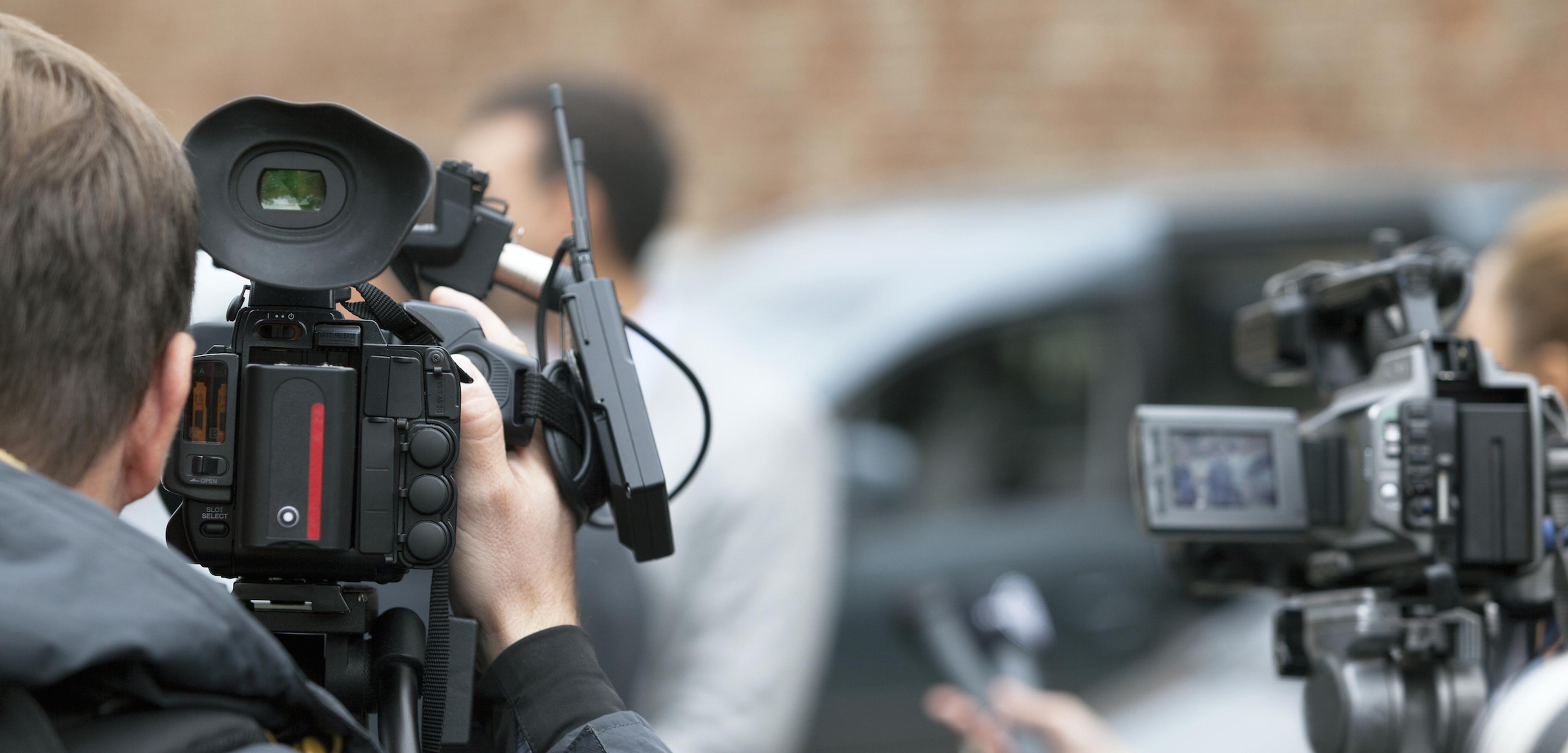 a man is holding a video camera in front of a group of people representing newsjacking
