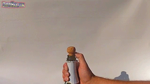 A hand holds a bottle with a cork, preparing to pop it open. The cork is about to be released, creating a celebratory moment.