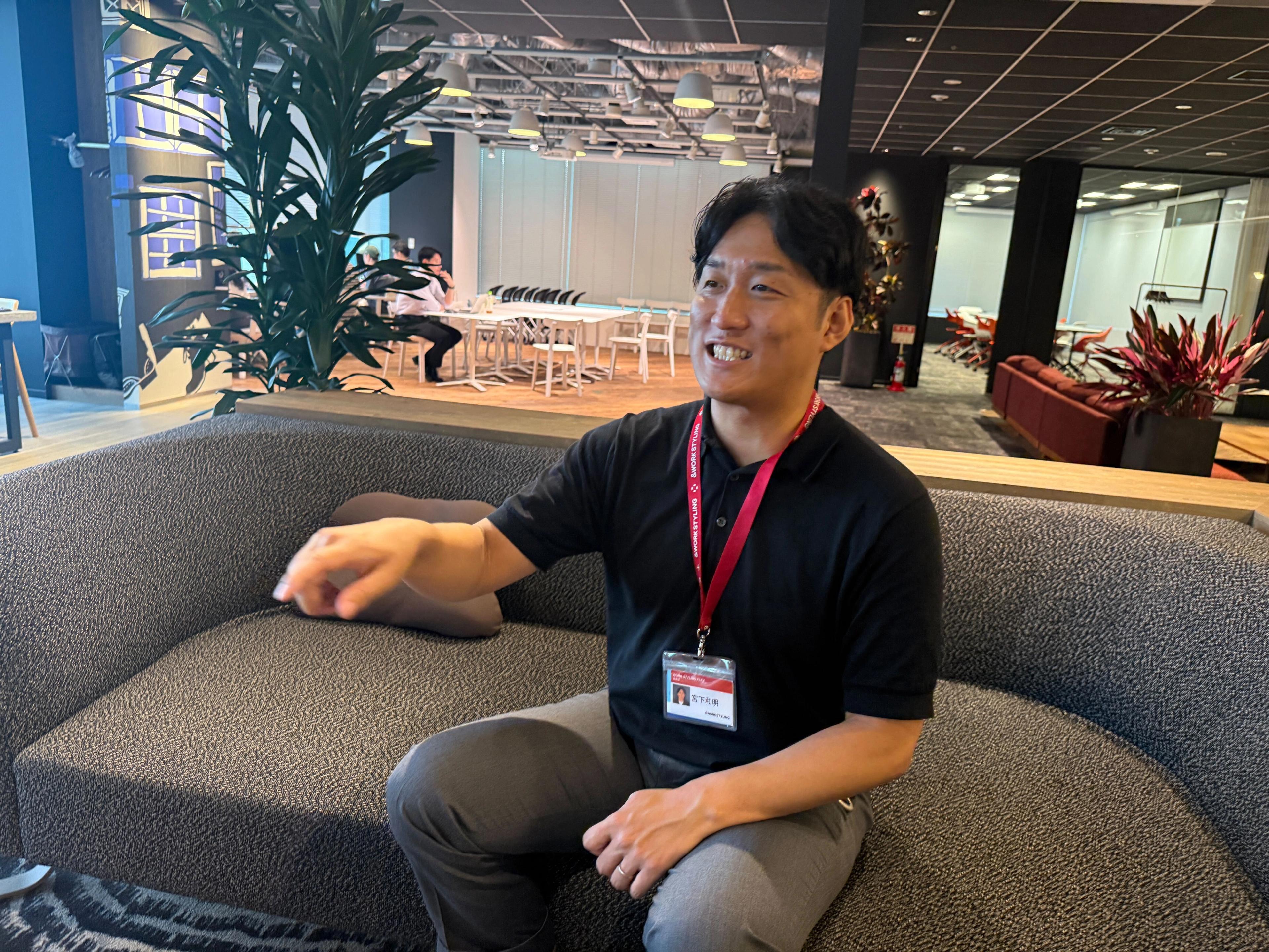 a man is sitting on a couch in an office and smiling .