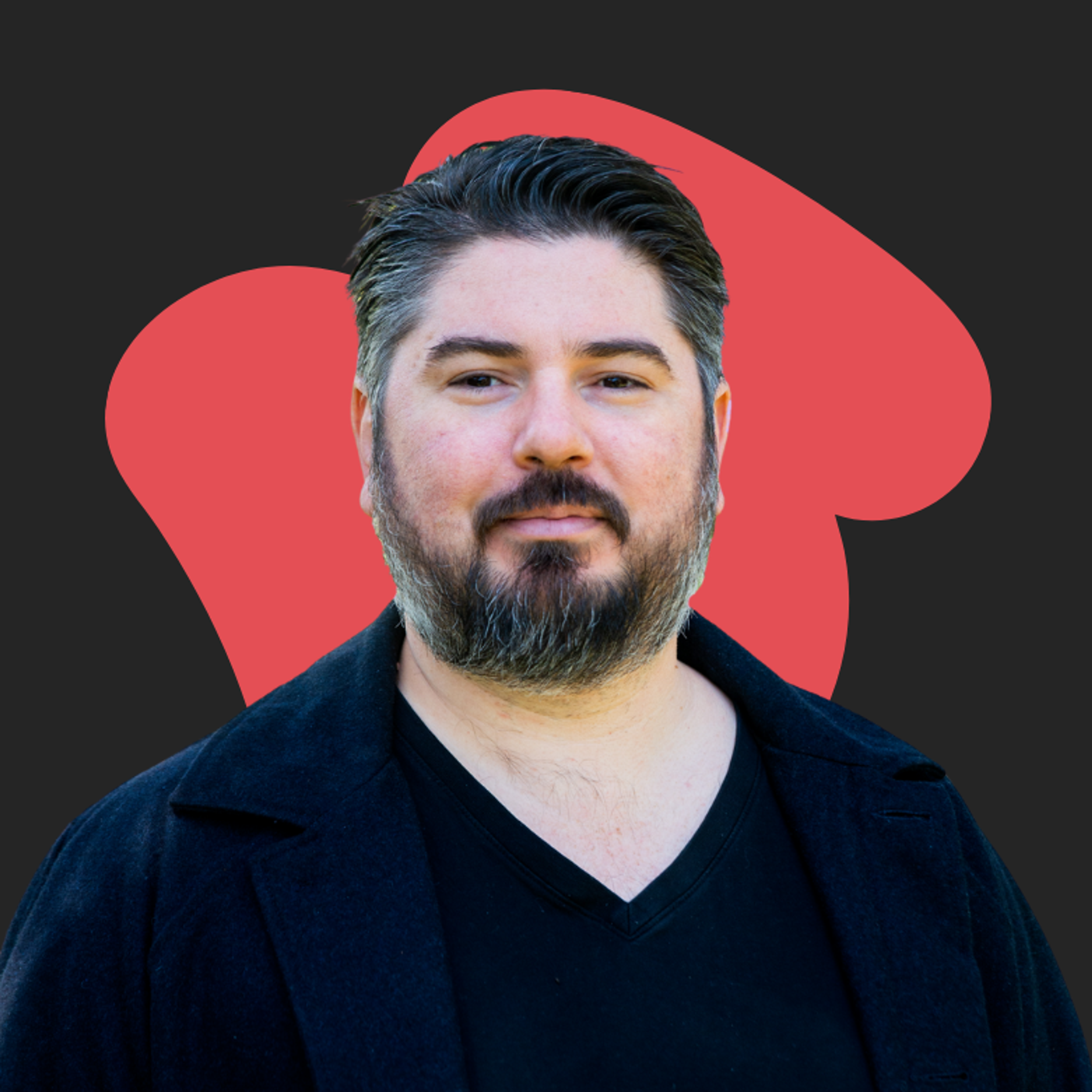 Bearded person with short dark hair wearing a black shirt and jacket, posing against a dark background with a red abstract shape.