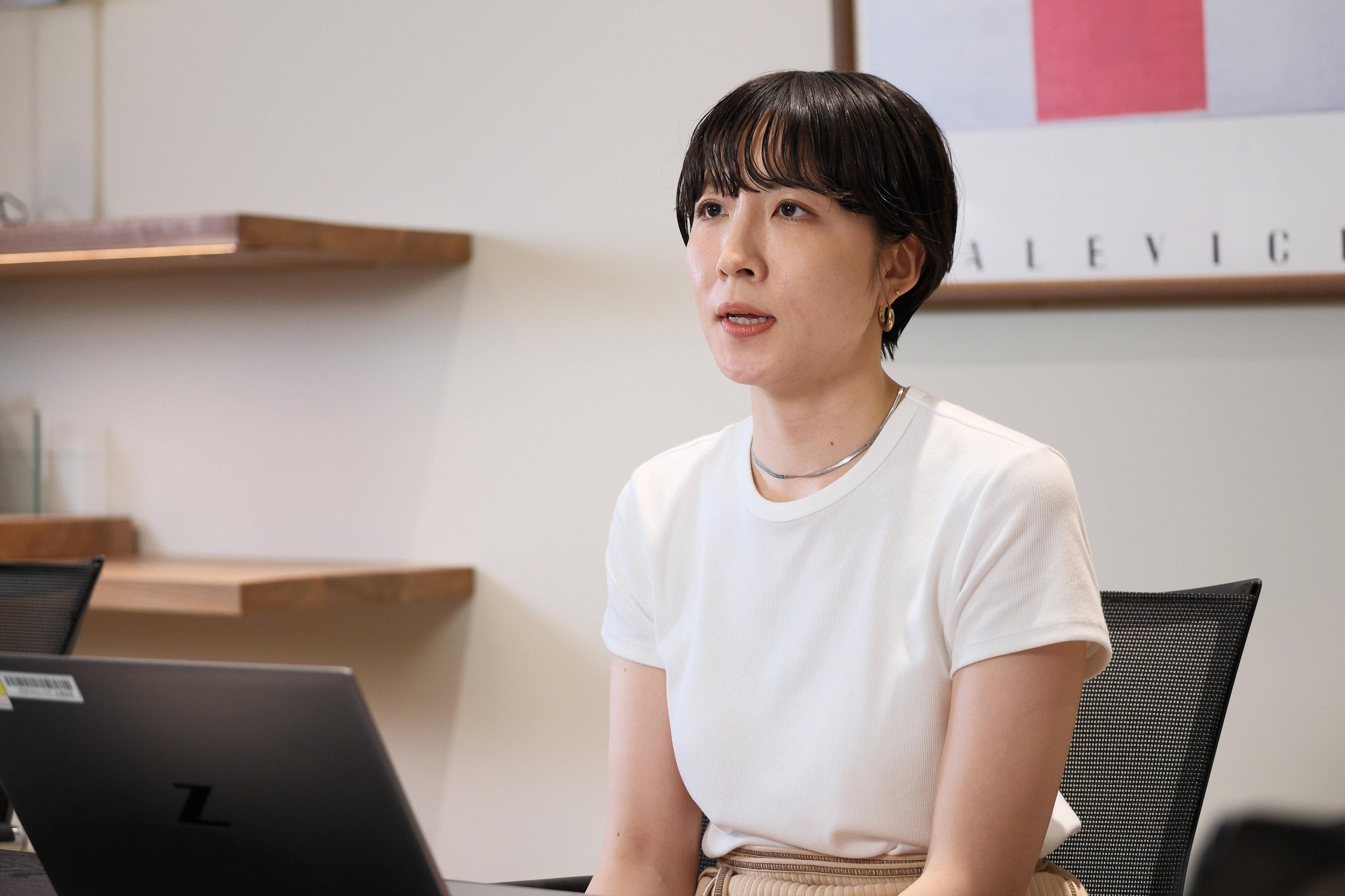 女性がパソコンの前に座り、話している様子。背景にはアート作品が飾られている。
