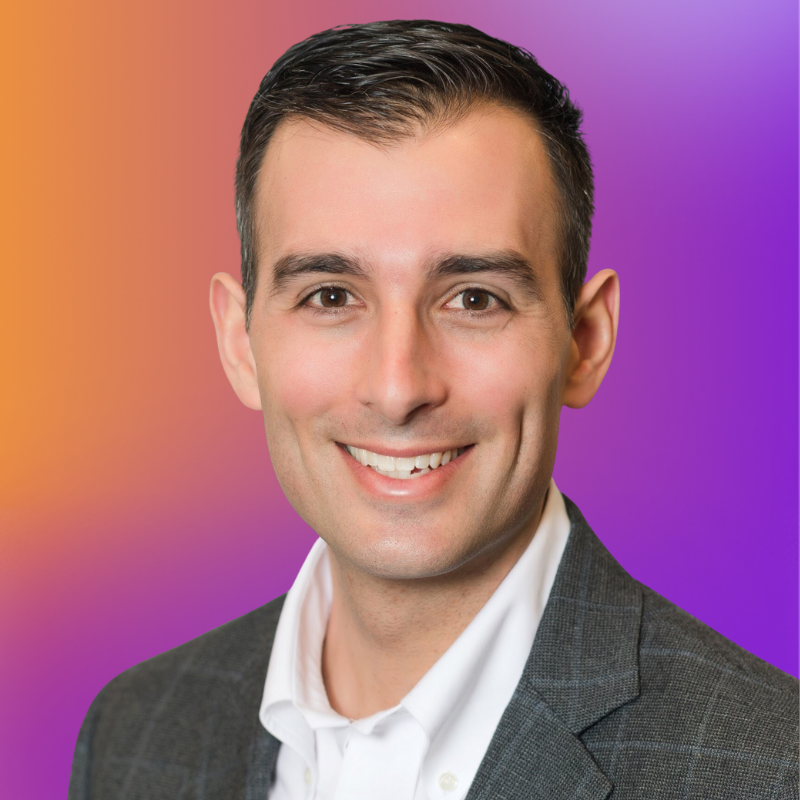 A smiling man in a gray blazer and white shirt against a gradient orange and purple background. He has short, dark hair and a friendly expression.
