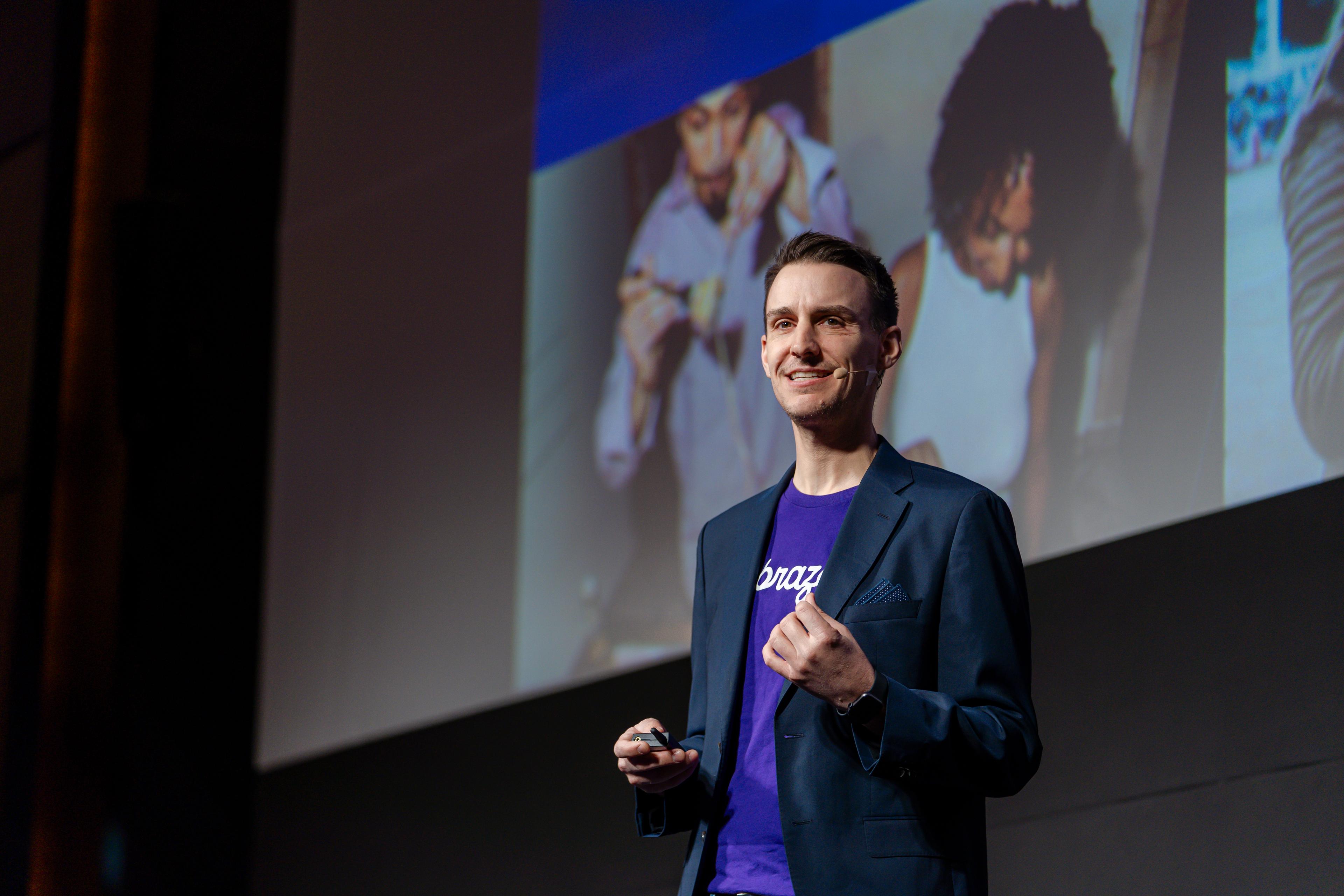a man in a suit and purple shirt is giving a speech on a stage .