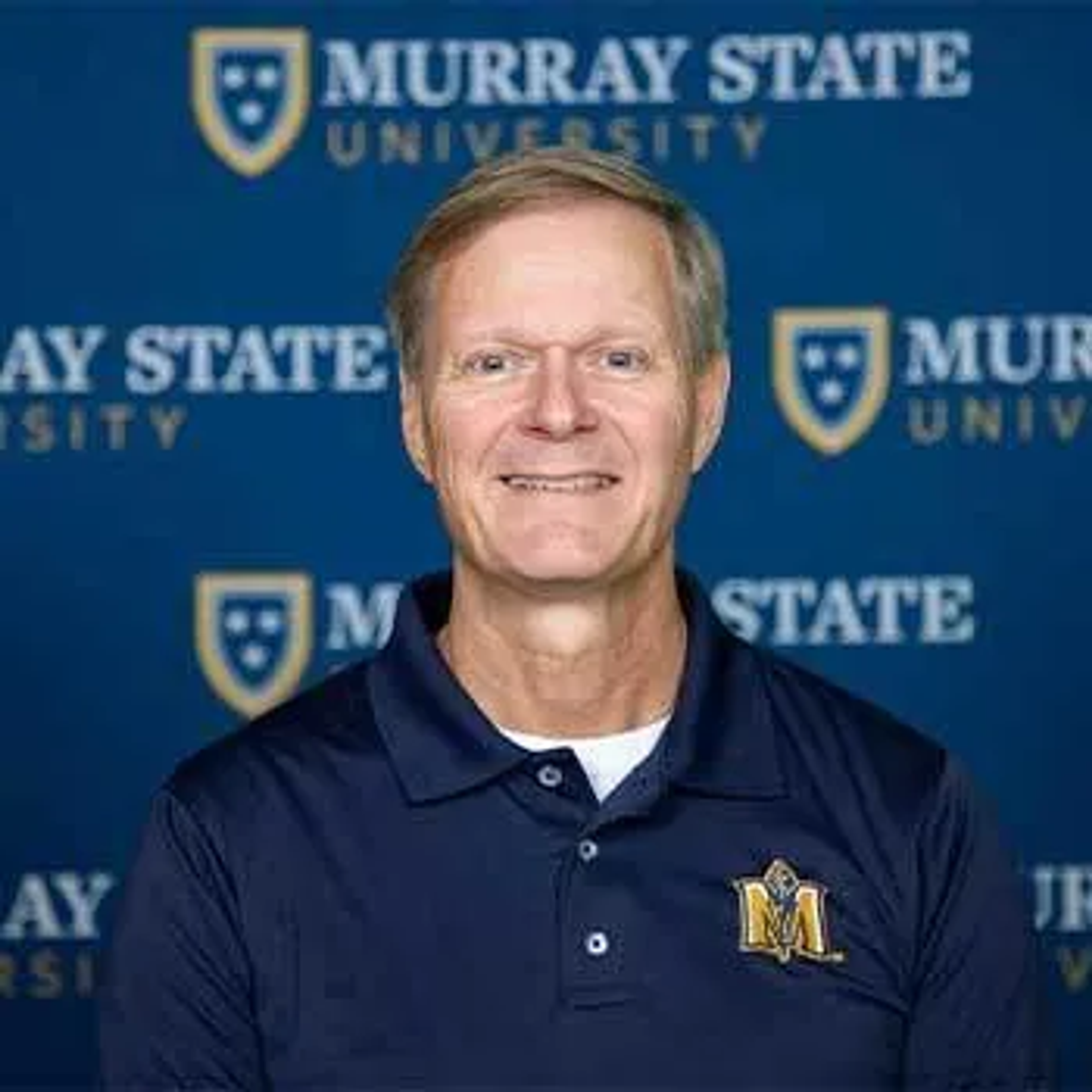 Smiling middle-aged man in a Murray State University polo shirt poses in front of a blue Murray State University backdrop.