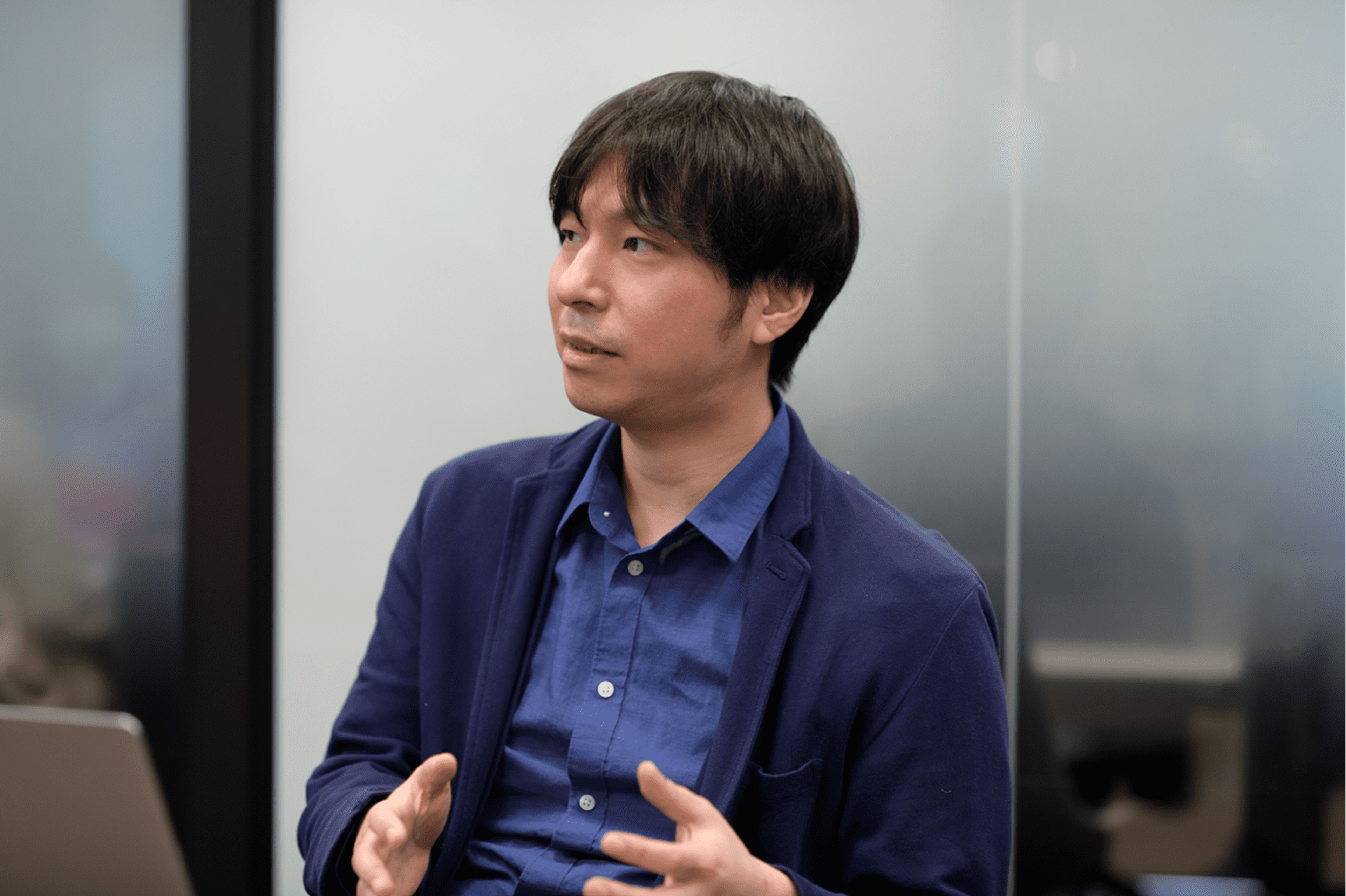 男性が会議室で話している様子。青いシャツとジャケットを着ています。