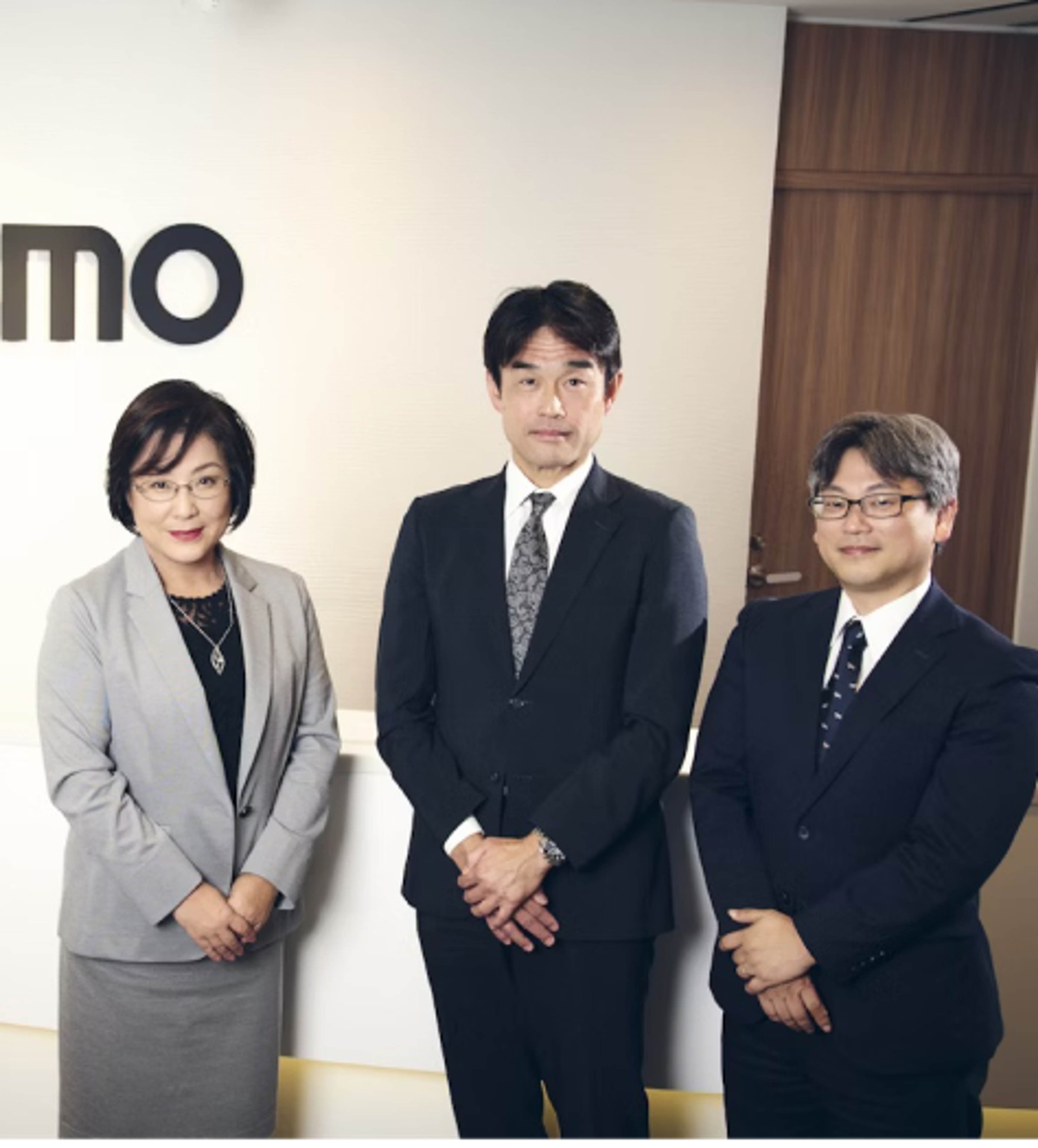 スーツを着た女性と男性二人が前にてをくんで立っている