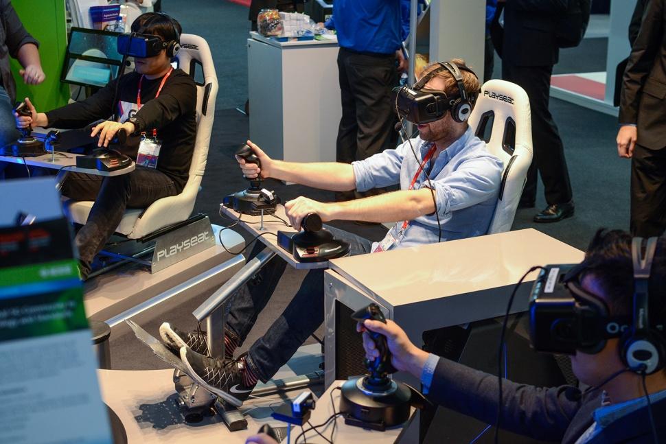 Two people are seated in gaming chairs wearing virtual reality headsets, engaged in a VR gaming experience. One person is using a flight simulator control setup.