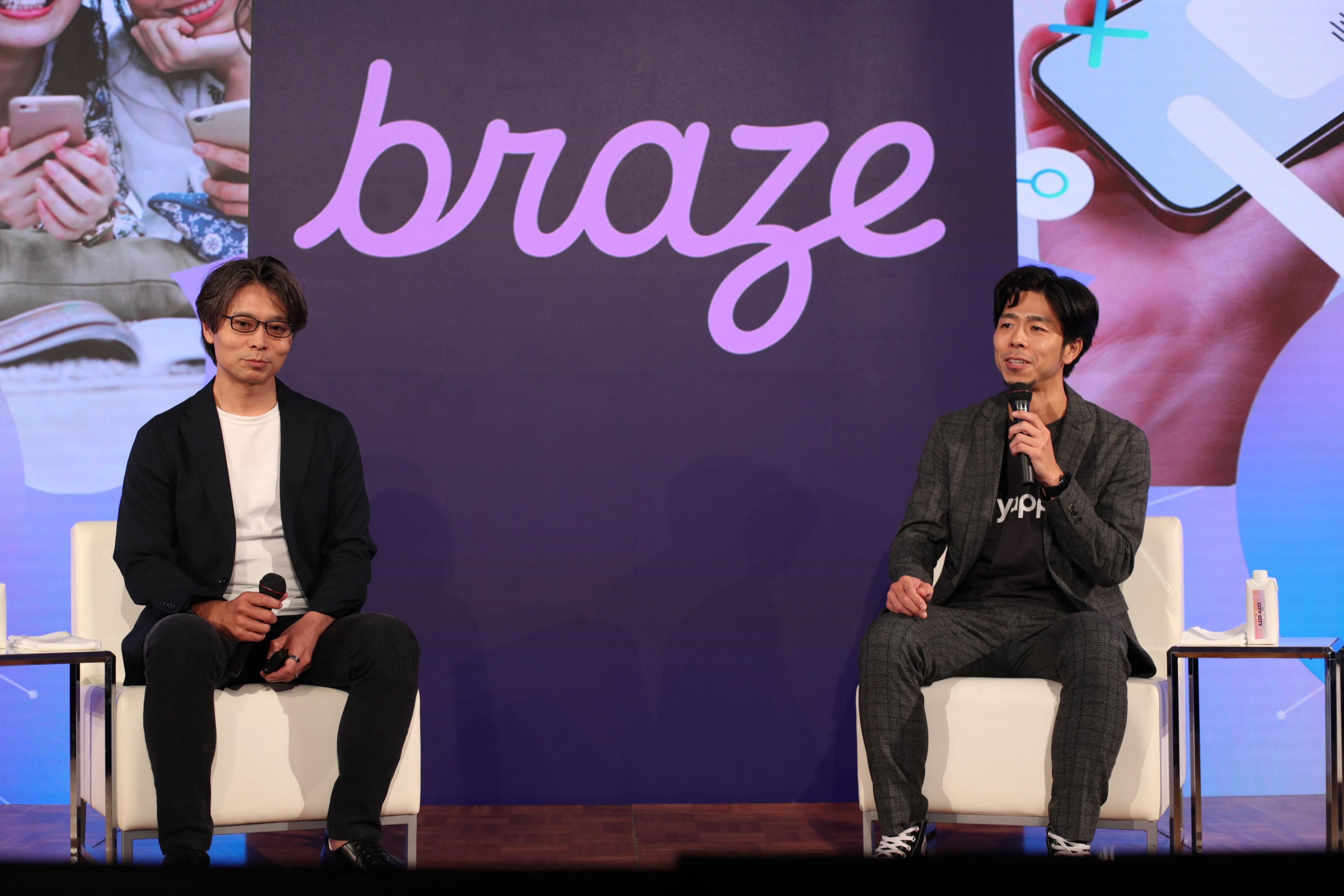紫色のbrazeのロゴを背景に、Brazeの新田と市川氏がステージに座り、マイクを使用して講演している画像
