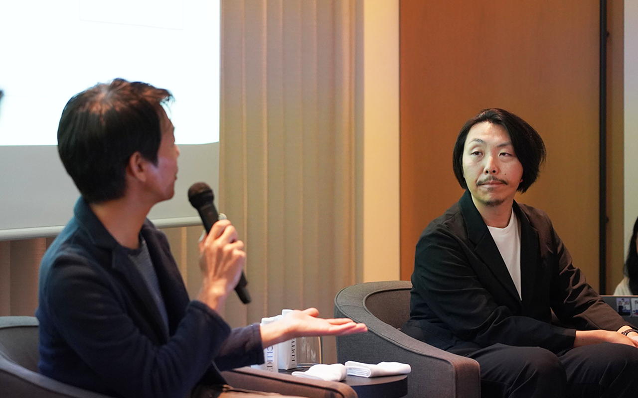 二人の男性が座って対話をしています。一人はマイクを持ち、話している様子です。