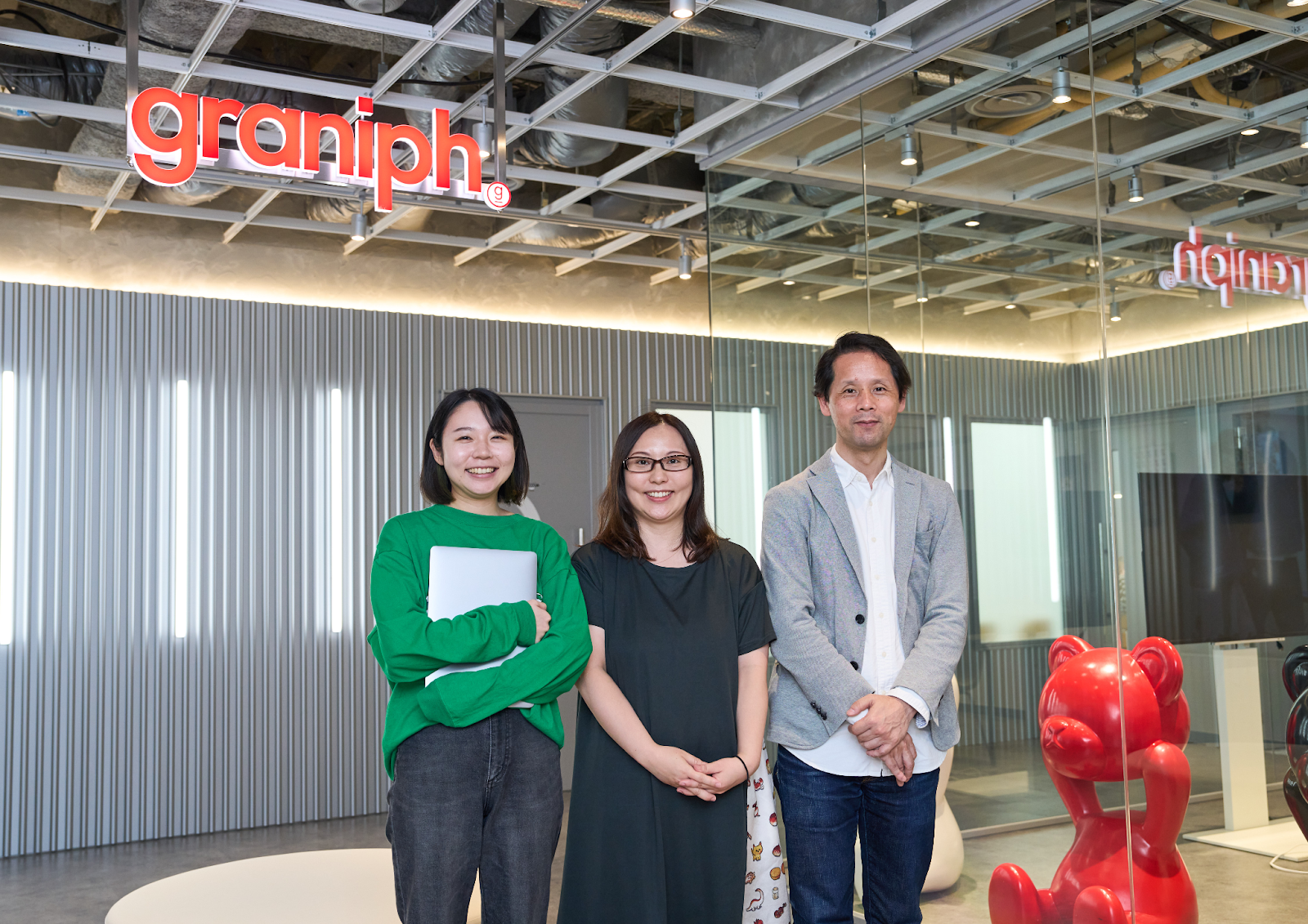 グラニフのオフィスで、3人の人が立っている。背景には「graniph」のロゴと赤いクマのオブジェが見える。