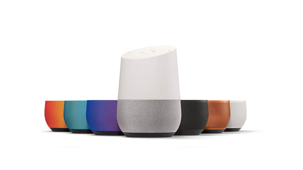 A collection of smart speakers in various colors, with one taller white speaker in the center and shorter colored speakers arranged around it.