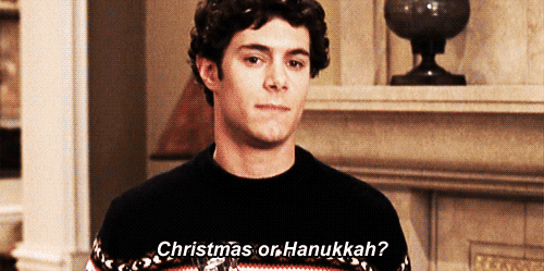 A young man in a festive sweater stands in a living room, looking contemplative. Text on the image reads, "Christmas or Hanukkah?