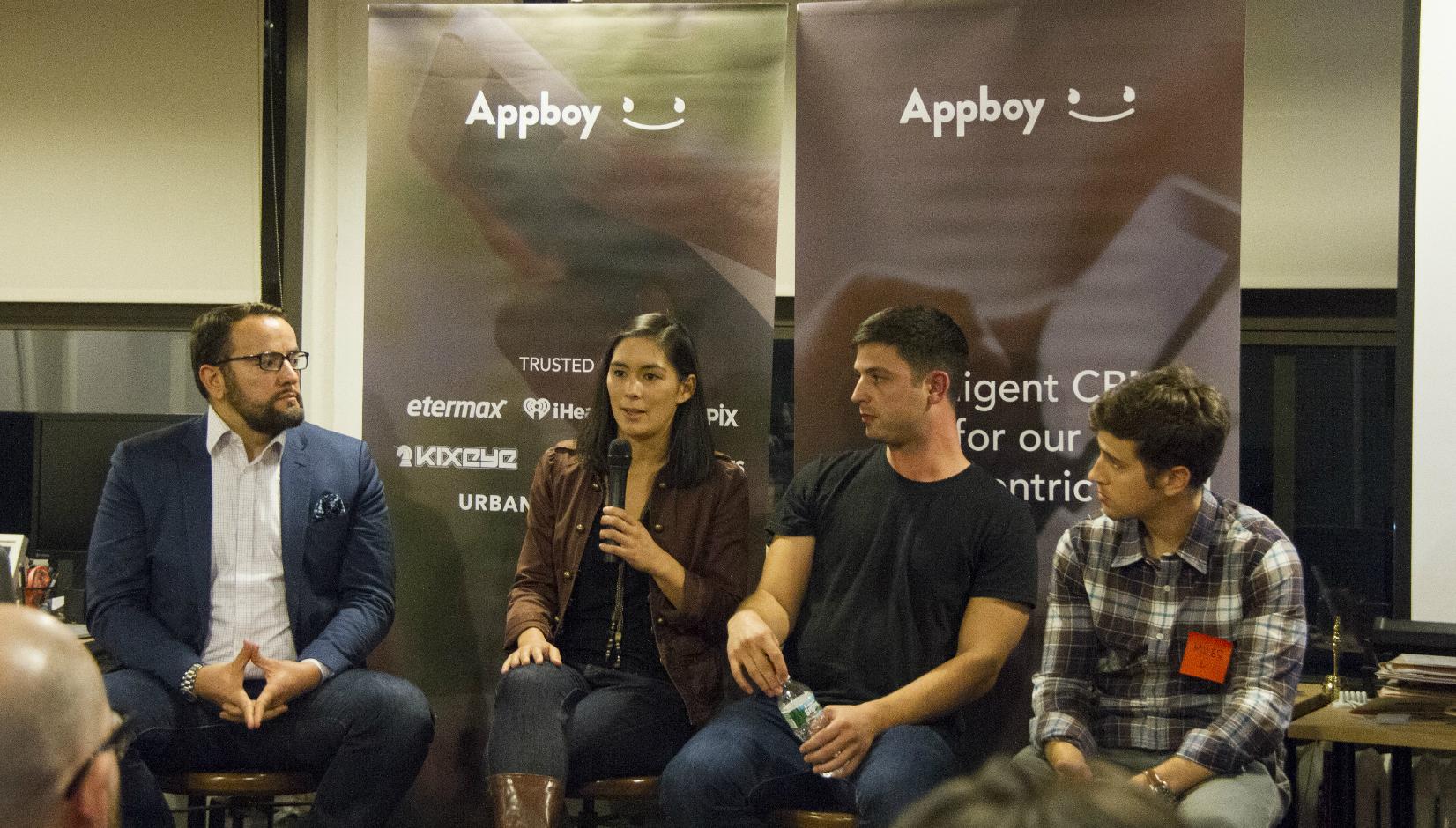 A panel discussion featuring four speakers seated in front of Appboy banners. One speaker is addressing the audience while the others listen.