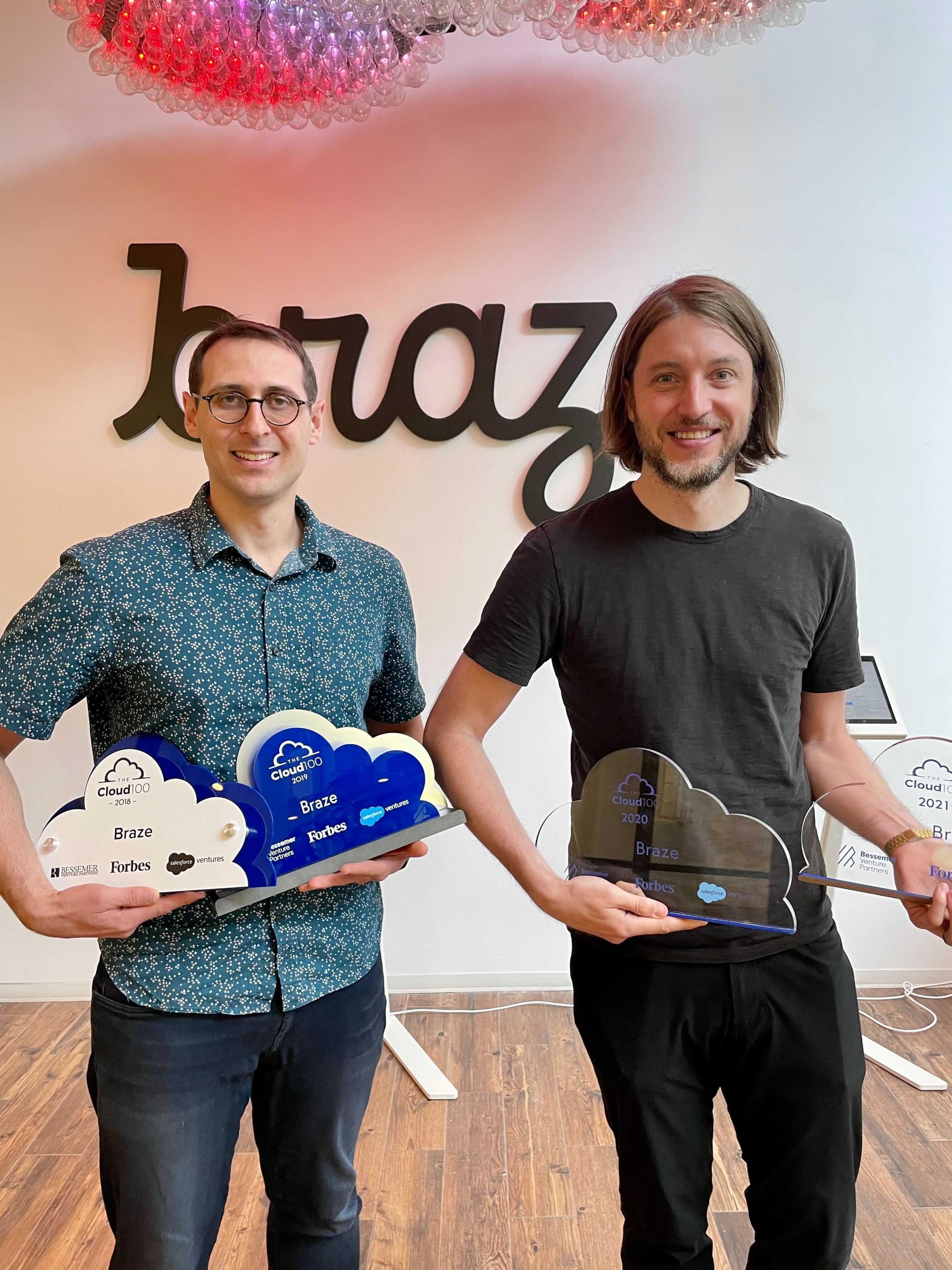 ブラゼのオフィスで、2人の男性が受賞トロフィーを持っています。背景には「braze」のロゴがあります。