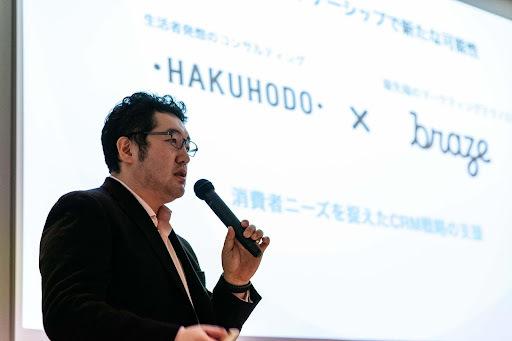 男性がマイクを持ってプレゼンテーションを行っている。背景には「HAKUHODO」と「braze」のロゴが表示されている。