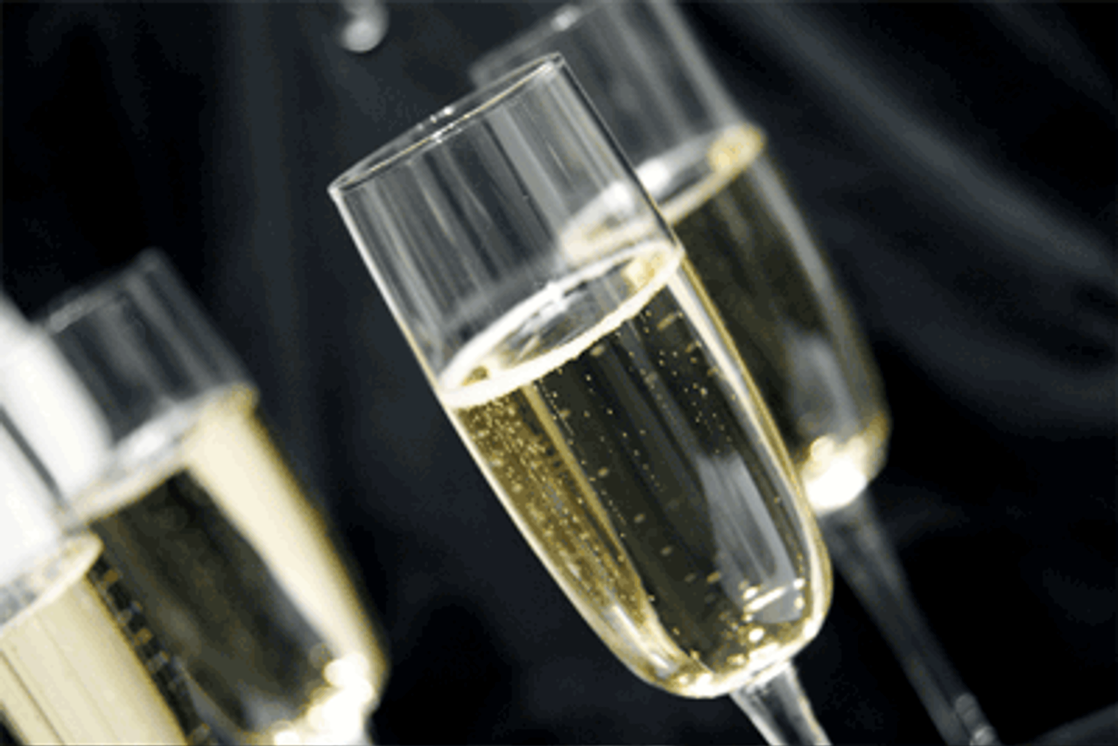 Four champagne flutes filled with sparkling champagne against a dark background. Bubbles rise in the glasses.
