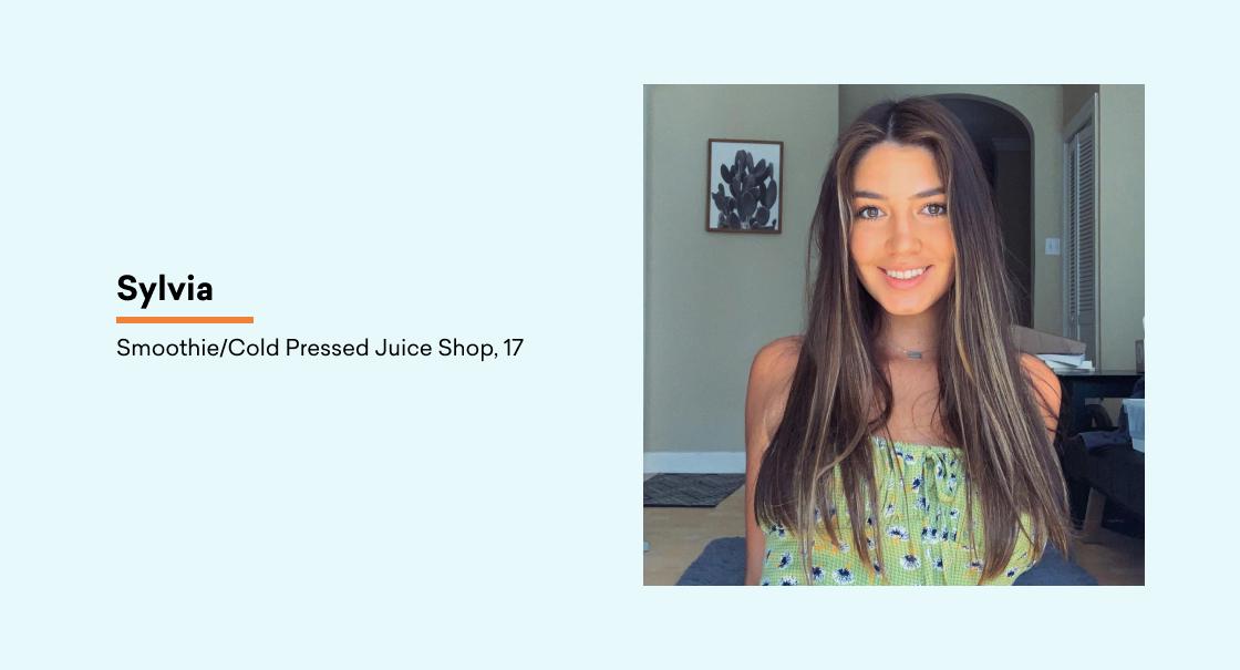 A young woman with long, straight hair smiles at the camera, wearing a green patterned top. The background features a light-colored wall and a plant.