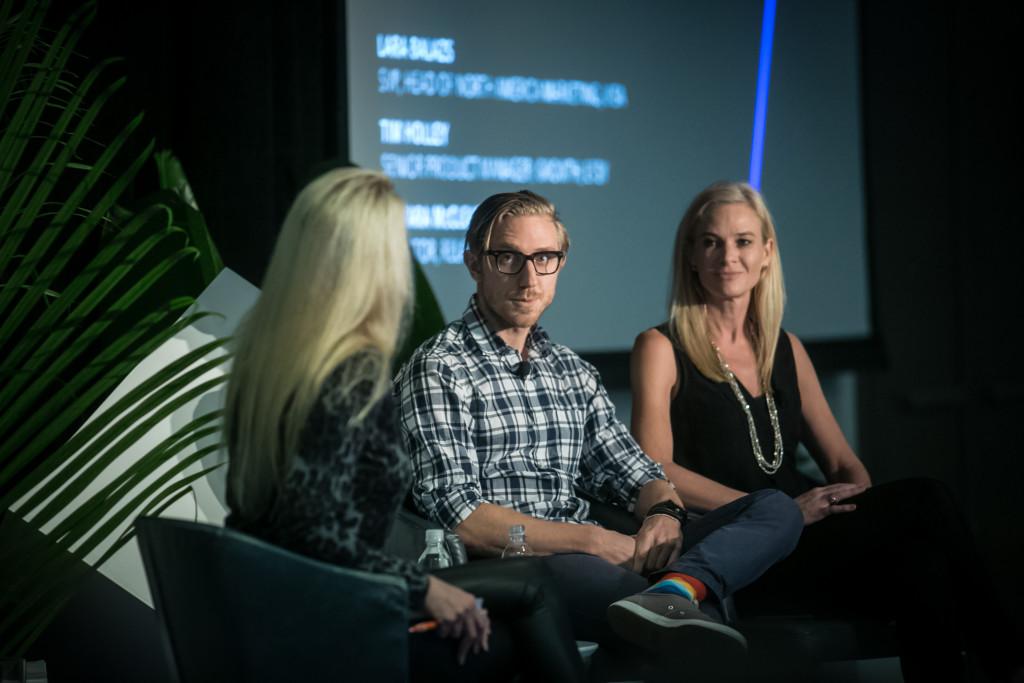 A panel discussion featuring three speakers seated on stage, with one speaker asking questions. The background displays text related to the event.
