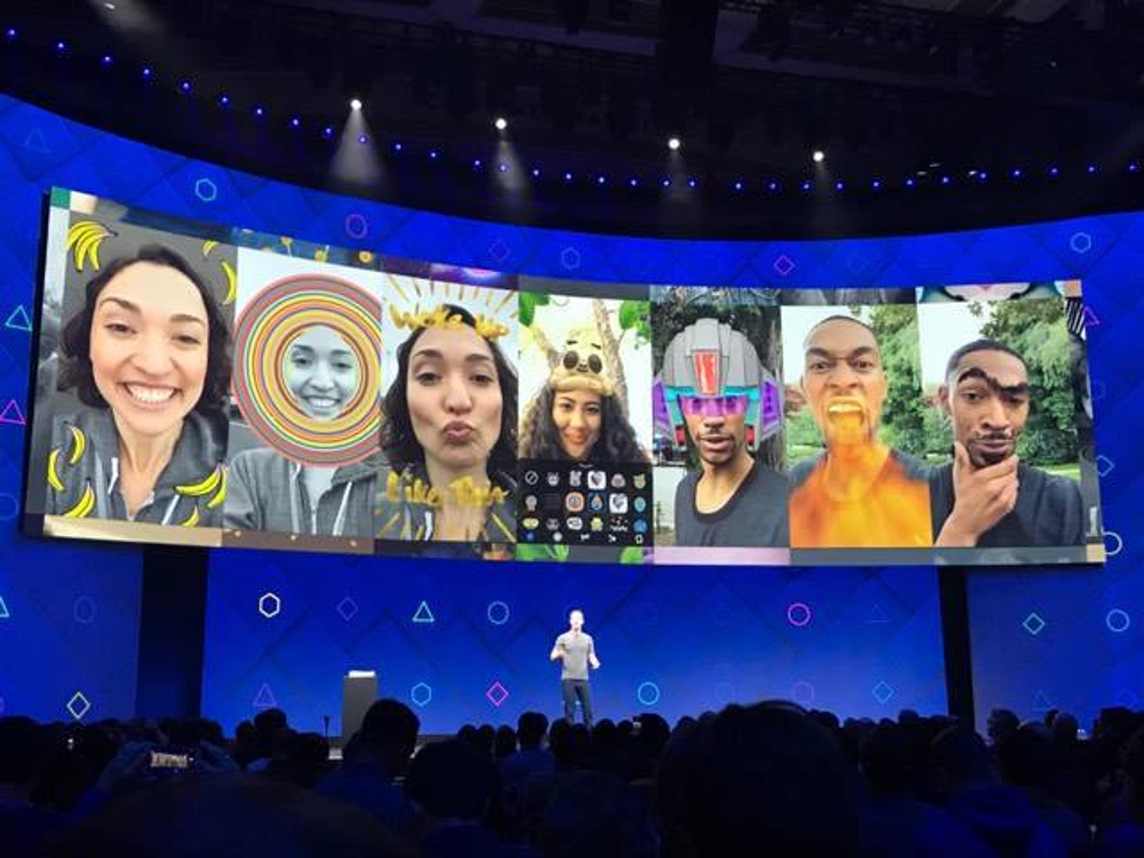 A person stands on stage in front of a large screen displaying various fun and colorful augmented reality filters applied to selfies. The audience is visible in the foreground.