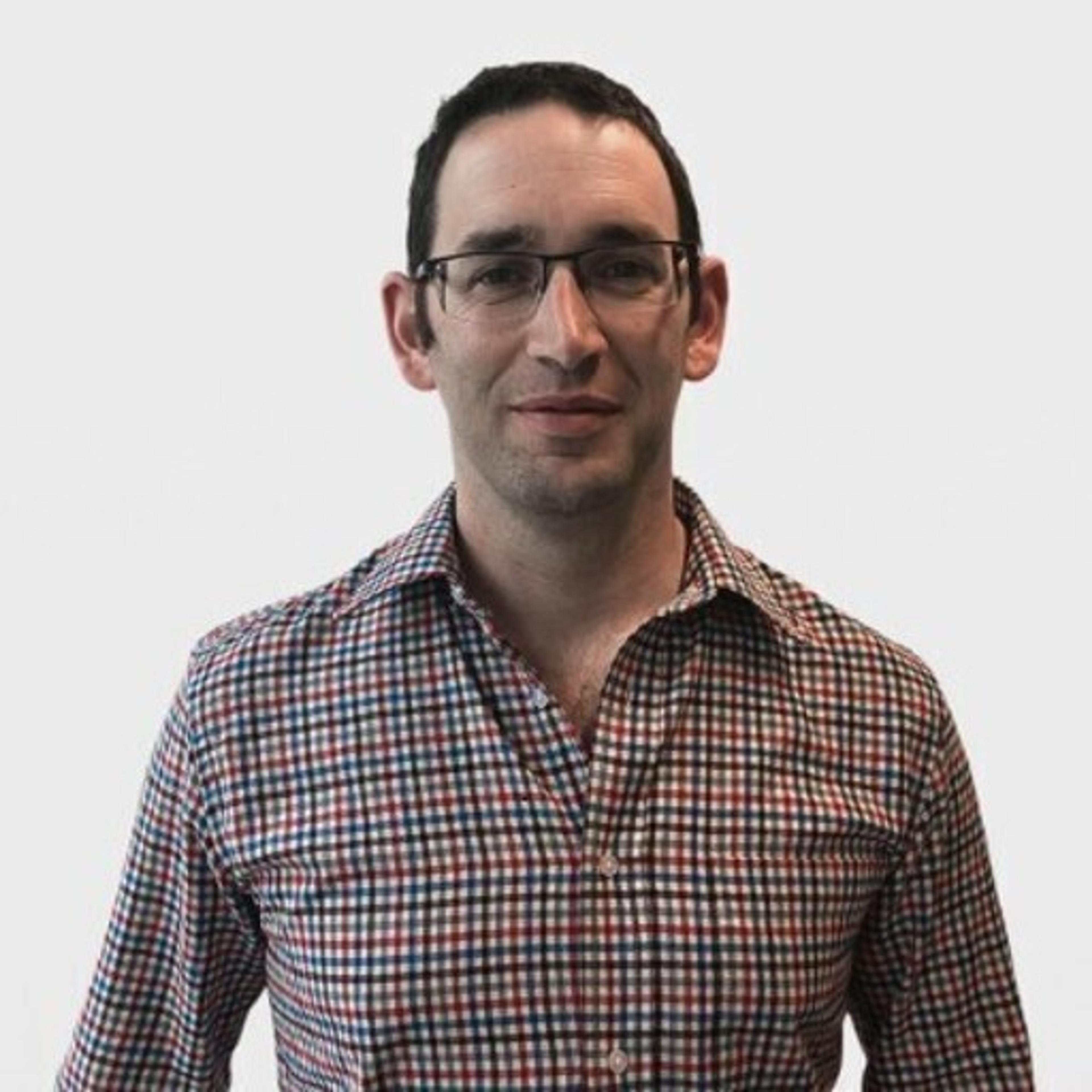 Headshot of a man wearing glasses and a checkered button-down shirt against a light gray background.