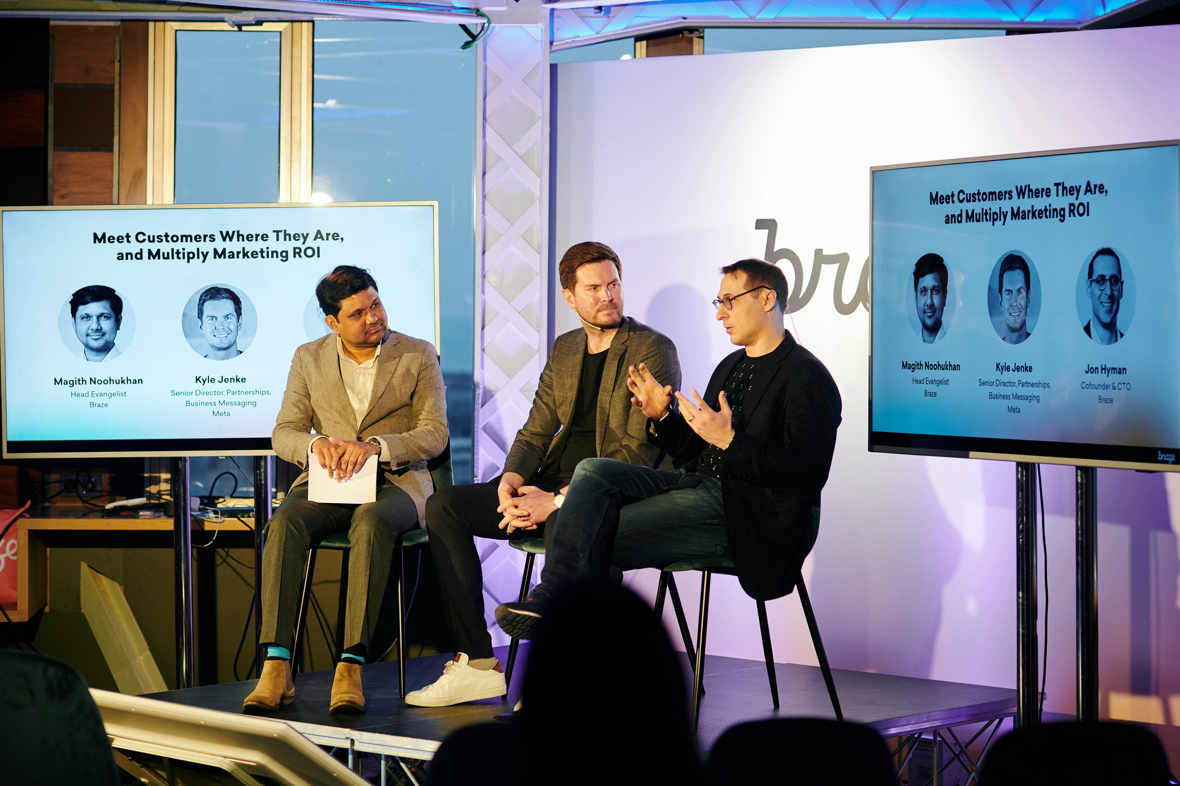 A panel discussion featuring three speakers discussing customer engagement and marketing ROI, with two screens displaying their names and the session title.