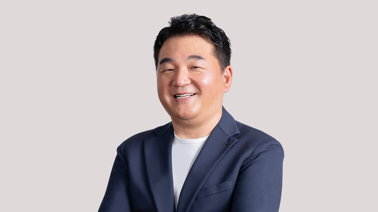 ビジネススーツを着た男性が微笑んでいる。背景は薄い色。