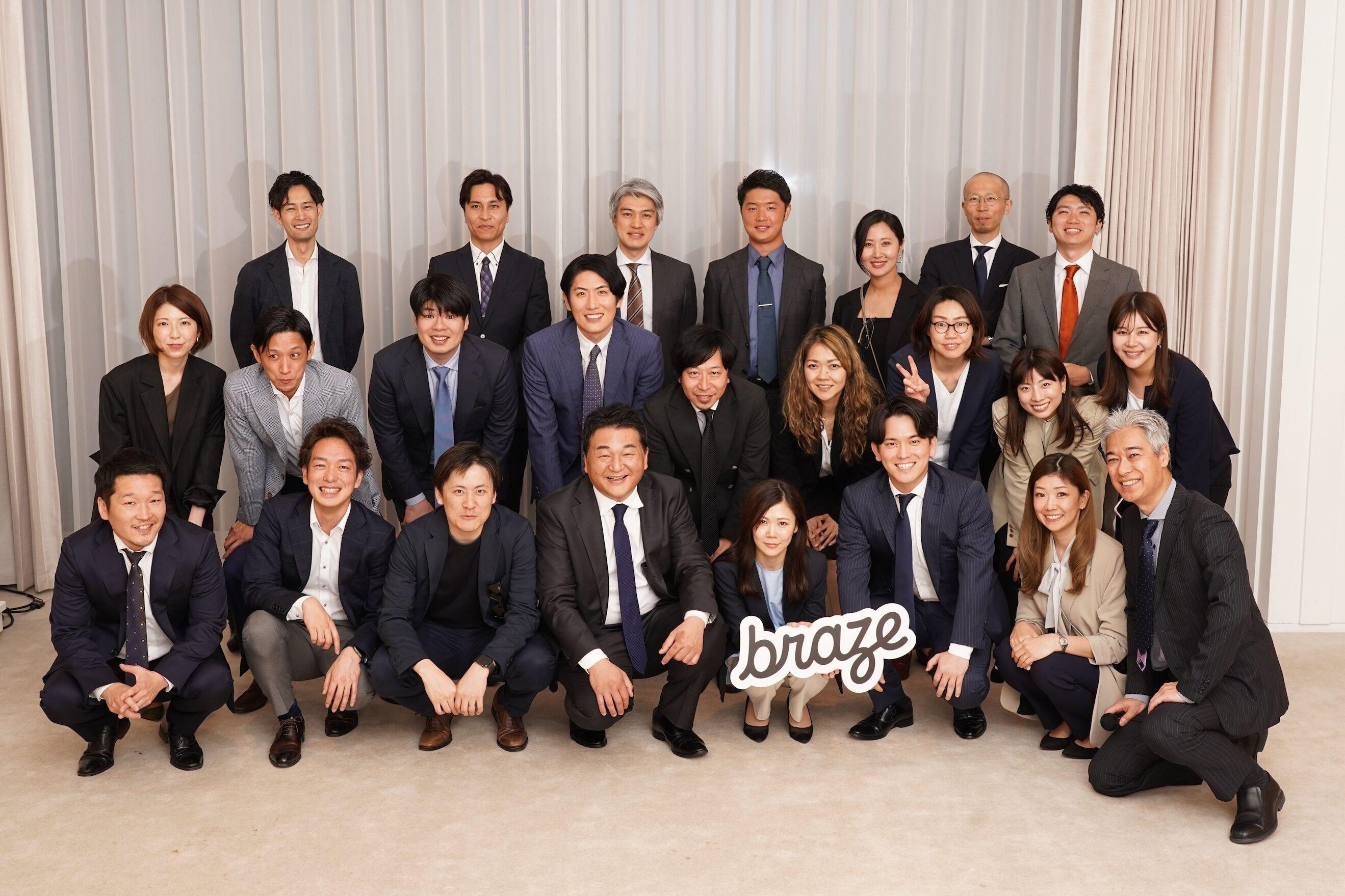 ビジネススーツを着た多くの人々が集まっているグループ写真。中央に「braze」のサインを持った人がいます。